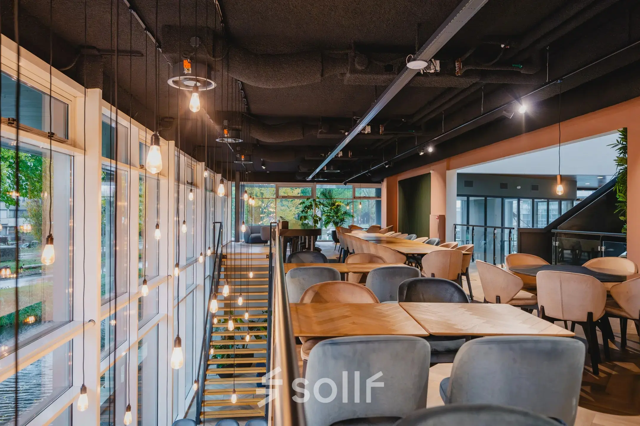 A stylishly furnished workspace at John M. Keynesplein, featuring contemporary seating and hanging lights, ideal for office space rental in Amsterdam Riekerpolder.