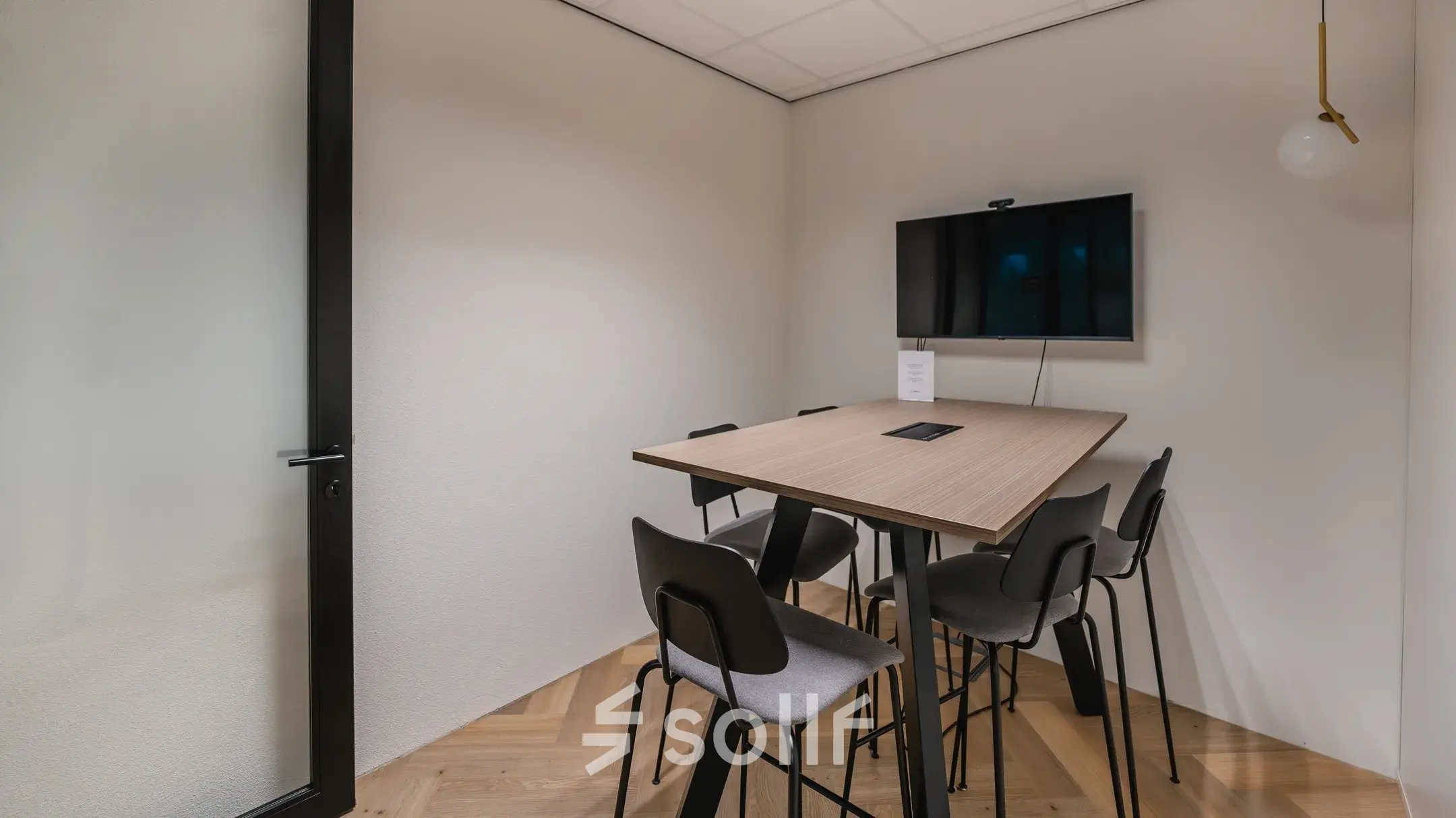 Modern office meeting space at John M. Keynesplein 4-10, Amsterdam Riekerpolder, featuring a table with chairs and a mounted screen for rent.