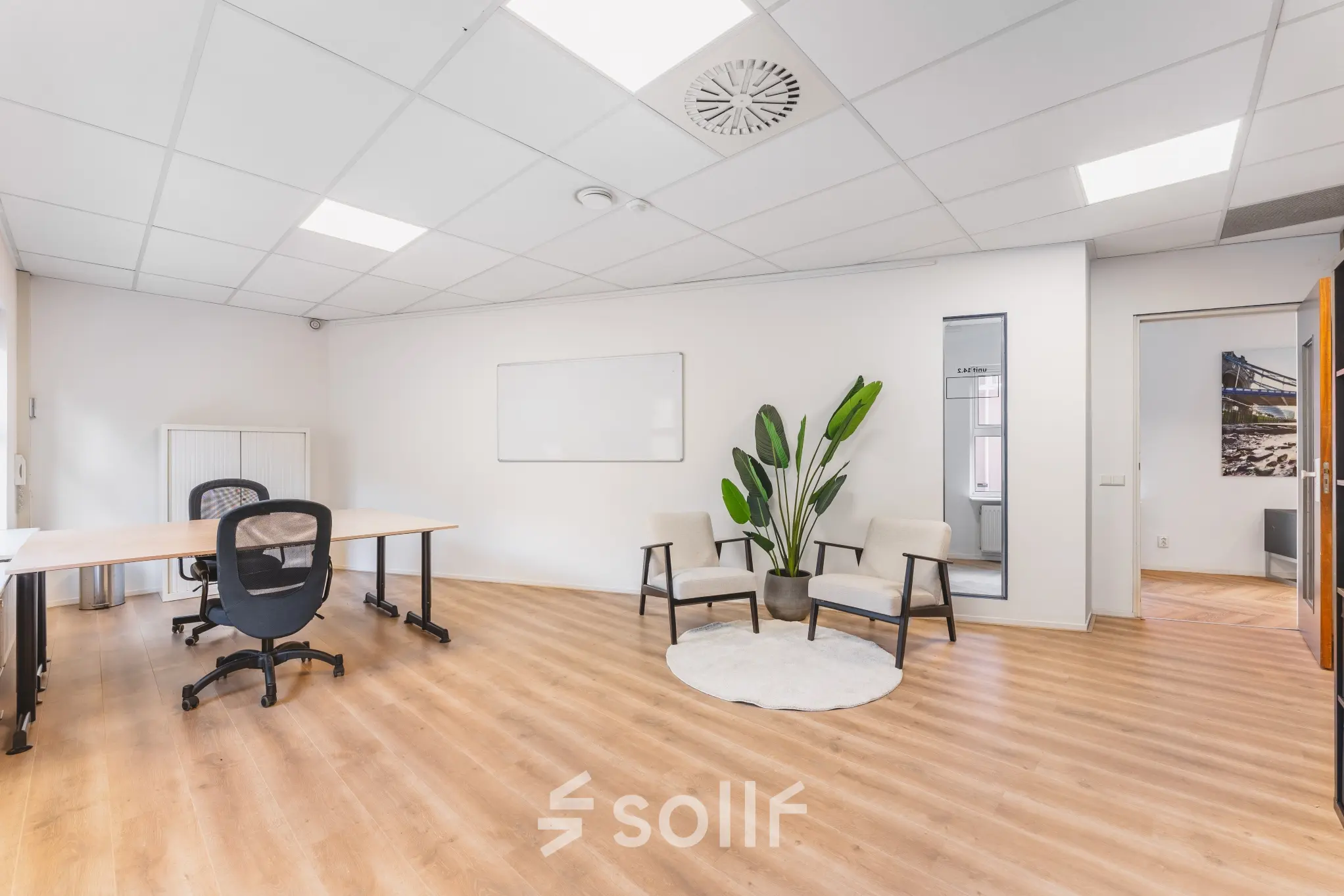 Bright office space with wooden flooring, two modern chairs, a desk with an office chair, and a potted plant. Ideal for office space rental in Amsterdam Sloterdijk.