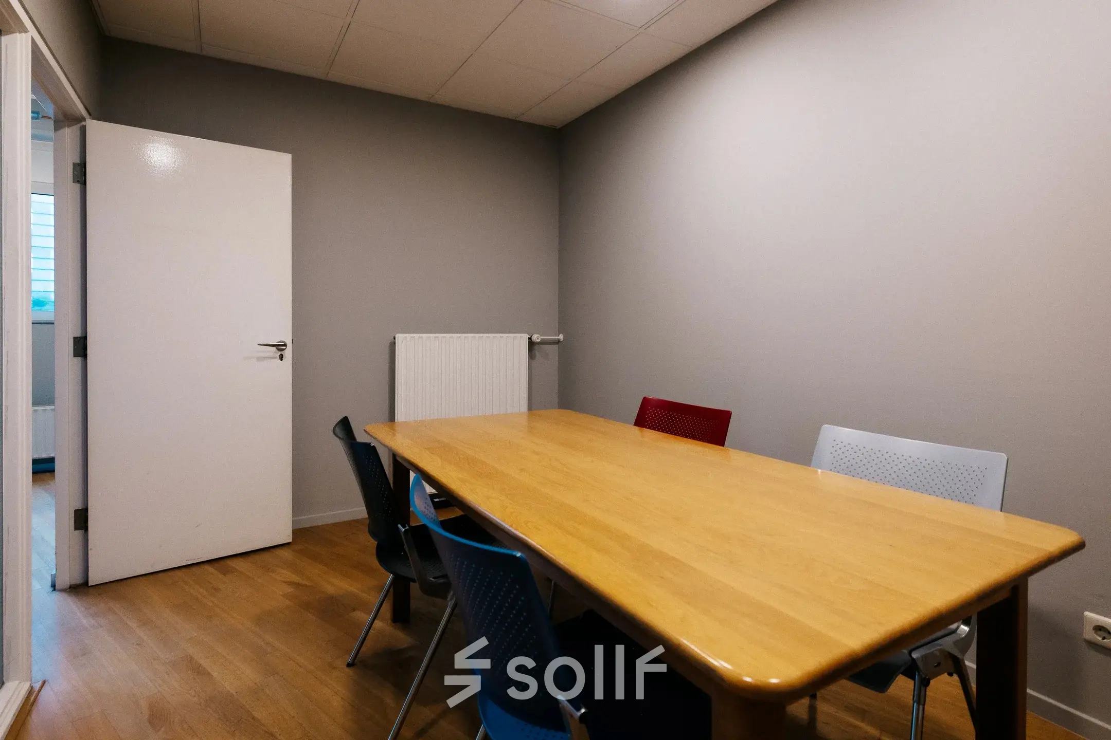 Compact conference room with a wooden table and colorful chairs, located at Kabelweg 24 in Amsterdam Sloterdijk, suitable for office space rental.