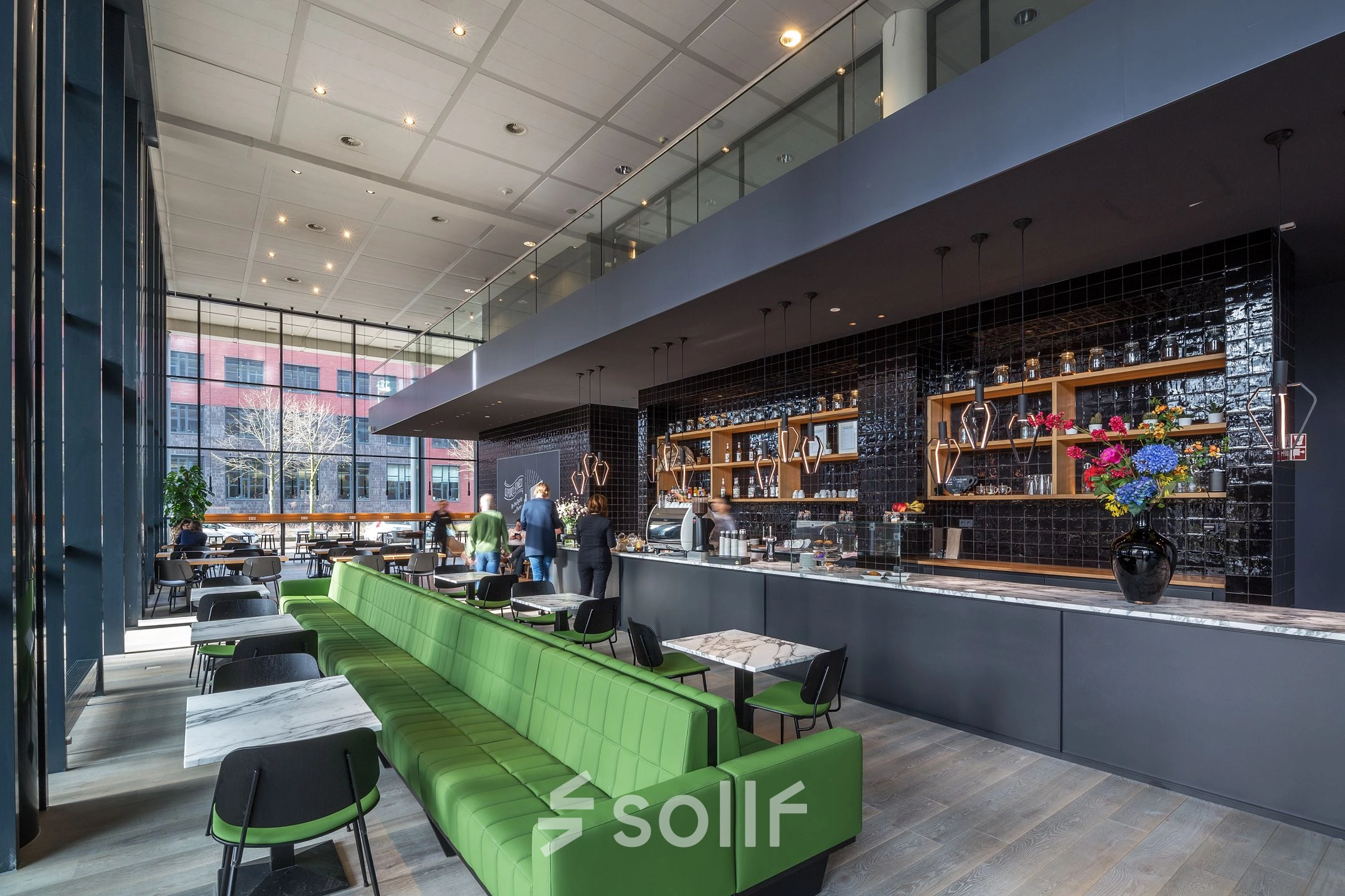 Modern office at Kingsfordweg 43, Amsterdam Sloterdijk, featuring an open lounge area with green seating and tables. People are engaged in conversation near the counter, enhancing the vibrant office space rental.
