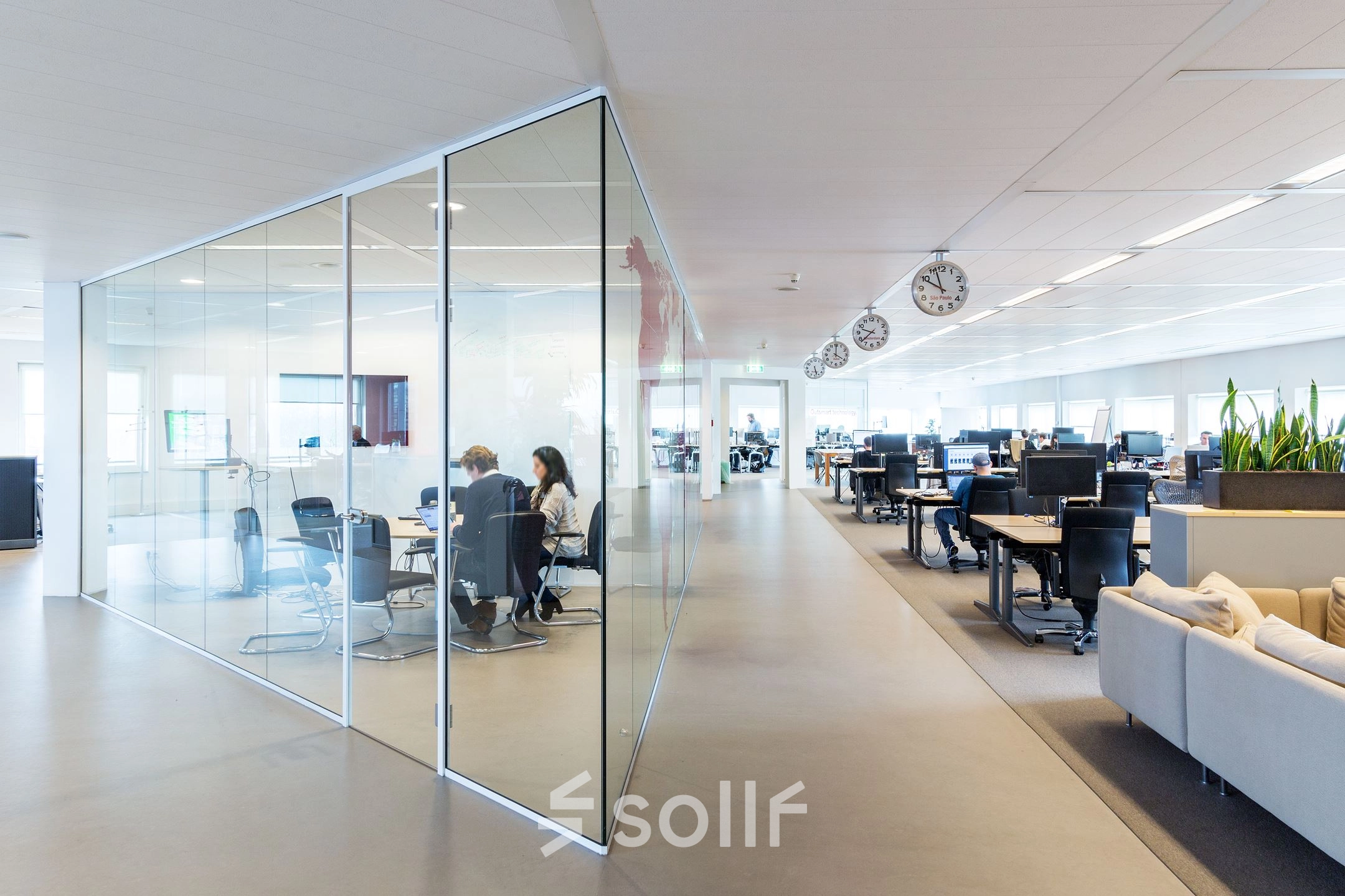 A modern office space at Kingsfordweg 43, Amsterdam Sloterdijk, featuring glass partitions and furnished workstations. People are engaged in meetings and working at desks, ideal for office space rental.