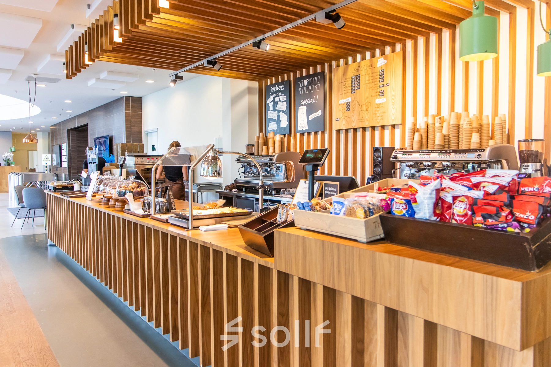 A welcoming pantry area at office space rental on Radarweg 29, Amsterdam Sloterdijk, featuring light wood decor and a variety of snacks for employees. A person is preparing coffee at a machine.