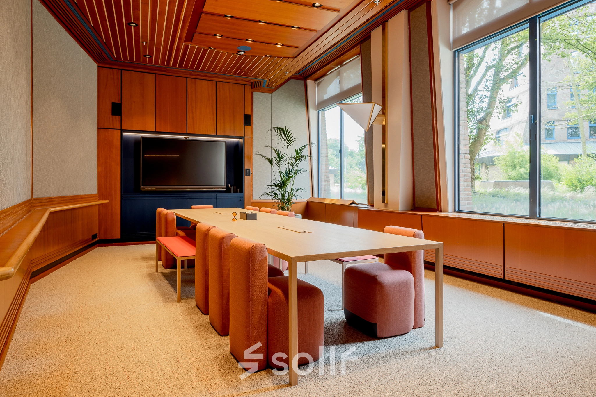 A furnished office space at Bijlmerplein 888, Amsterdam South East, featuring a wooden conference table and chairs with a large window view, ideal for rent office space needs.