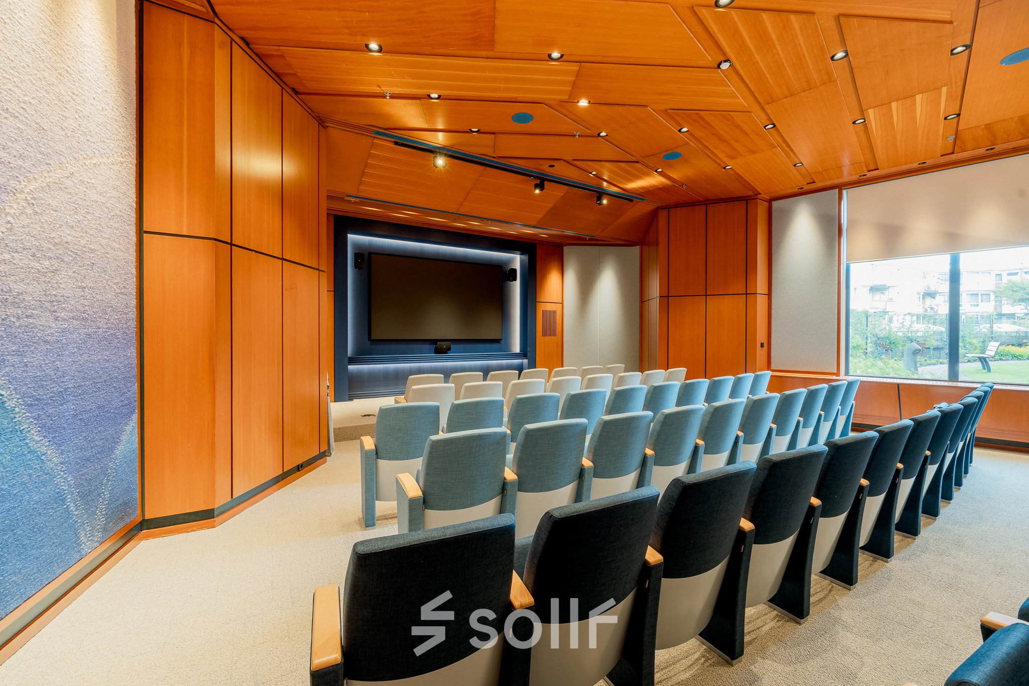 Seminar room at Bijlmerplein 888 in Amsterdam South East, featuring rows of cushioned chairs and a large presentation screen, ideal for office space rental.