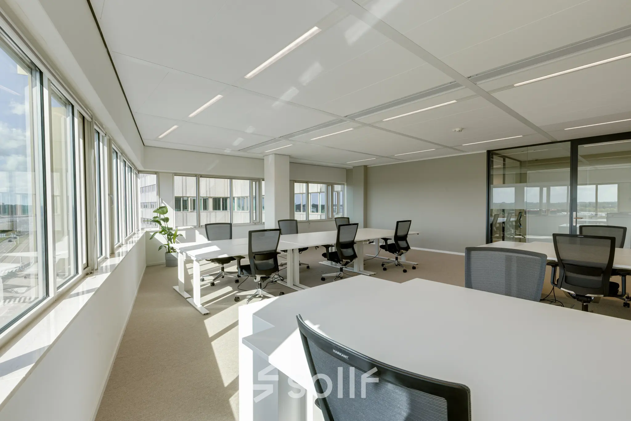 Bright office space rental in Amsterdam South East, featuring multiple desks and chairs with large windows allowing natural light.