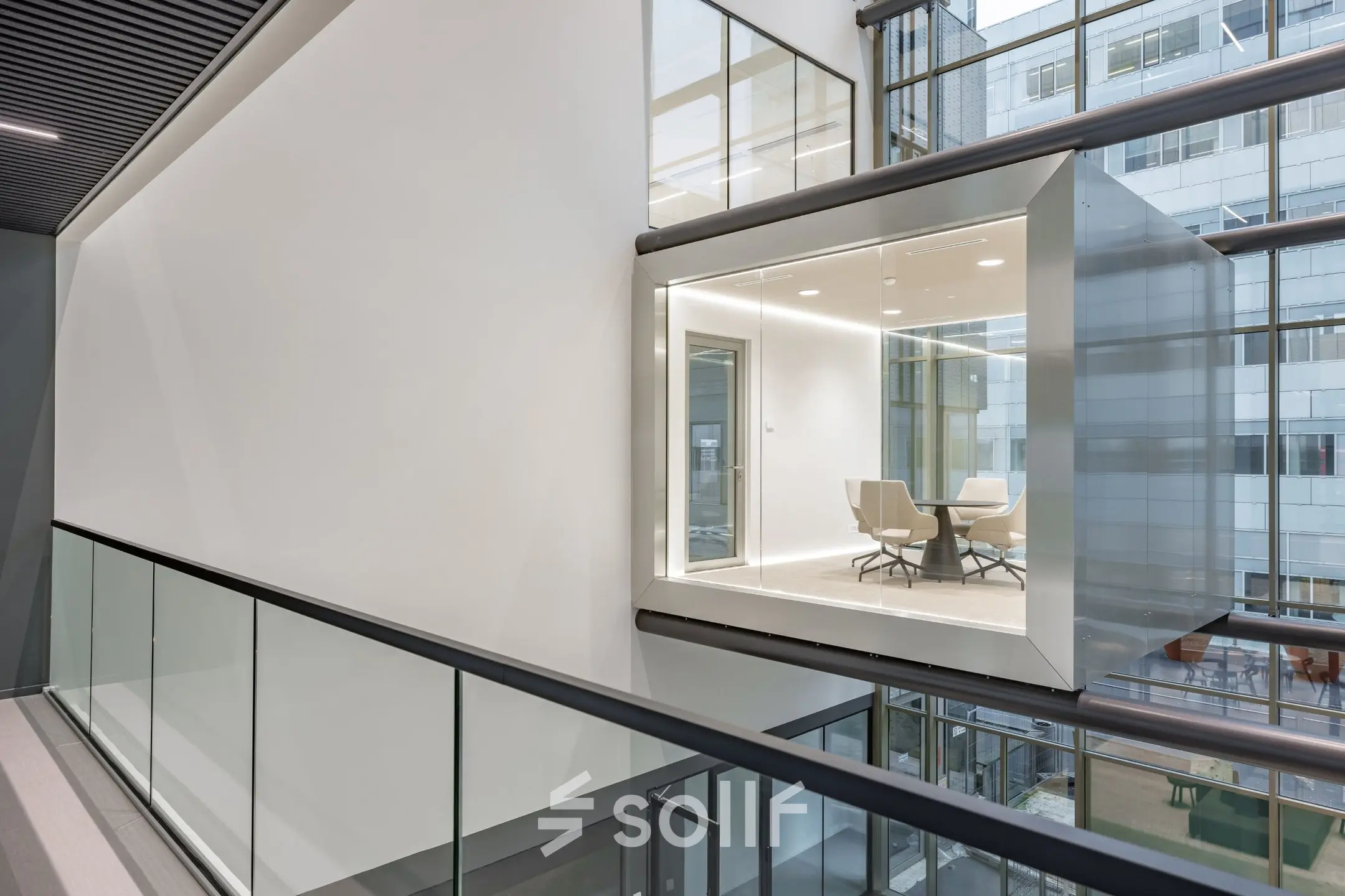 Modern office to rent at Herikerbergweg 290, Amsterdam South East, featuring sleek, glass-enclosed workspaces overlooking the building's atrium, ideal for office space rental.