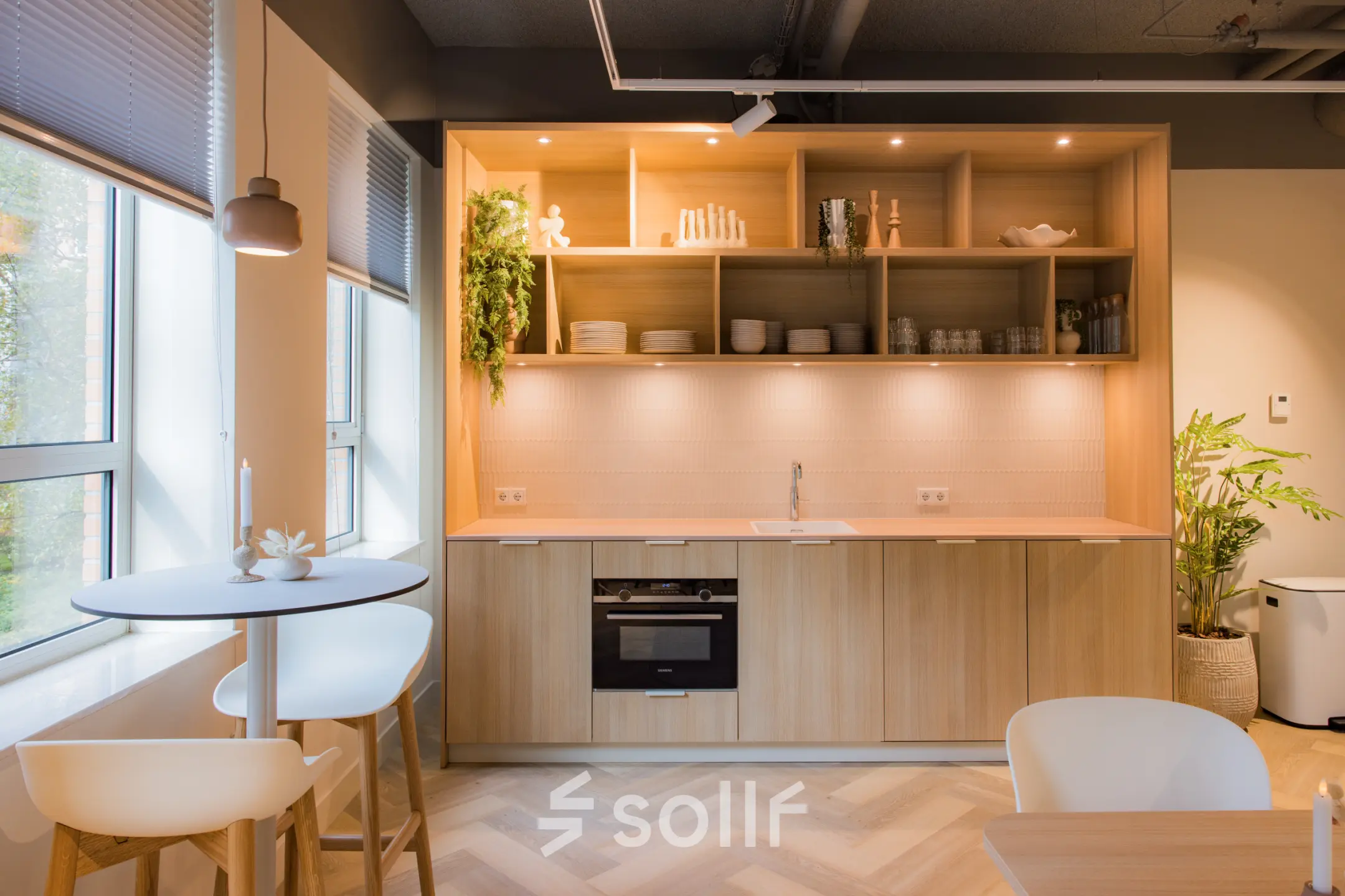 Modern furnished pantry with light wood cabinets, open shelves, and a small round table. Ideal for office space rental in Amsterdam South East.