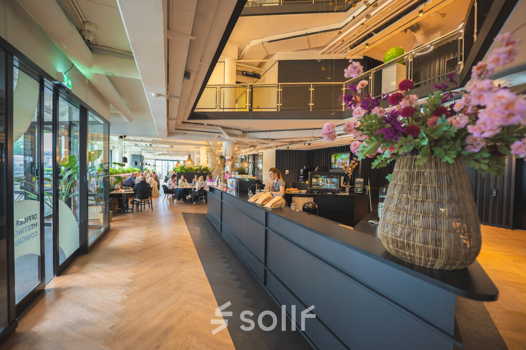 Modern office space for rent at Luttenbergweg 8, Amsterdam South East, featuring a stylish reception with people engaged in business discussions.