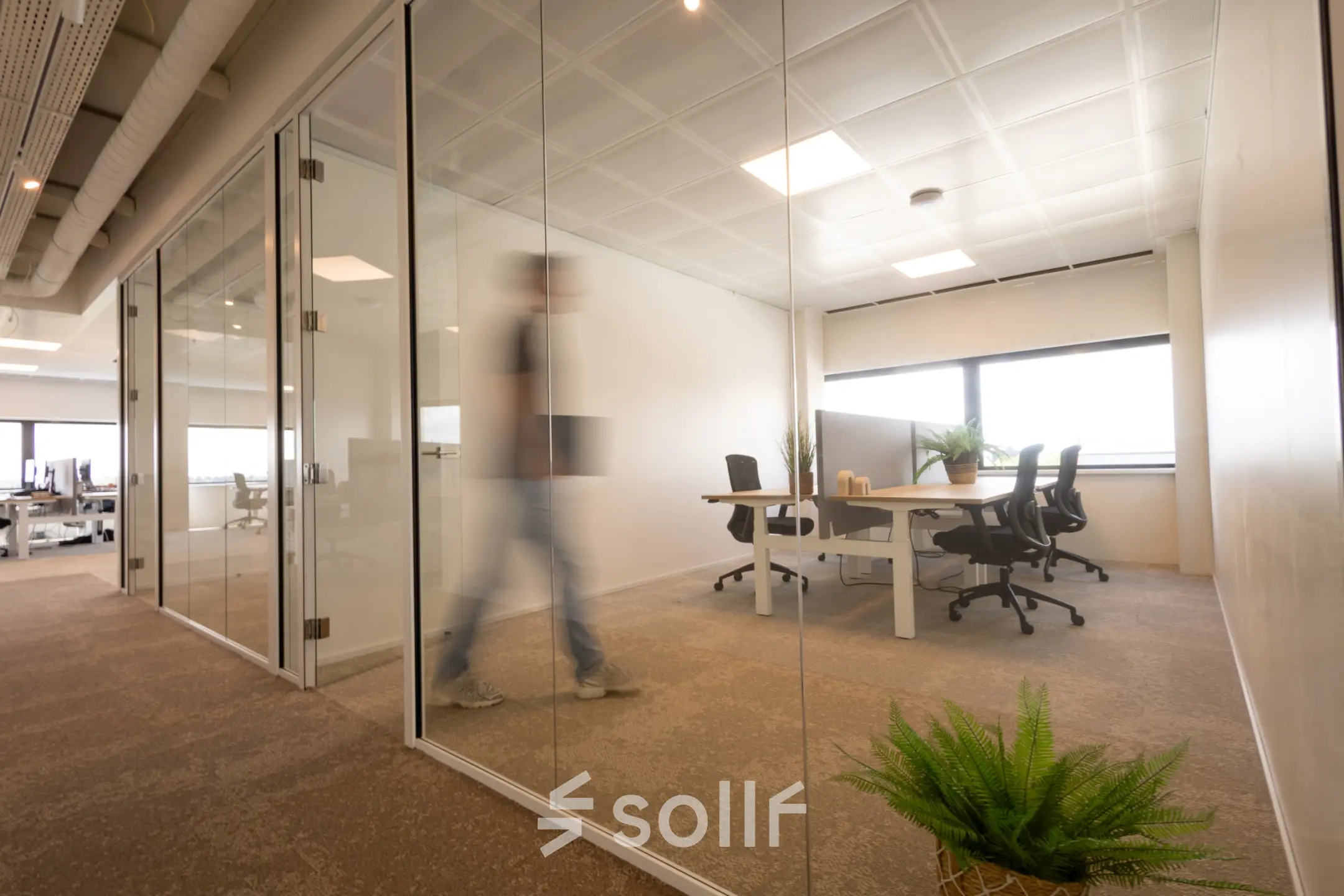 Modern office space at Luttenbergweg 8 in Amsterdam South East, featuring glass partitions, minimalist furnishings, and people working at desks. Ideal office space rental for collaborative work.