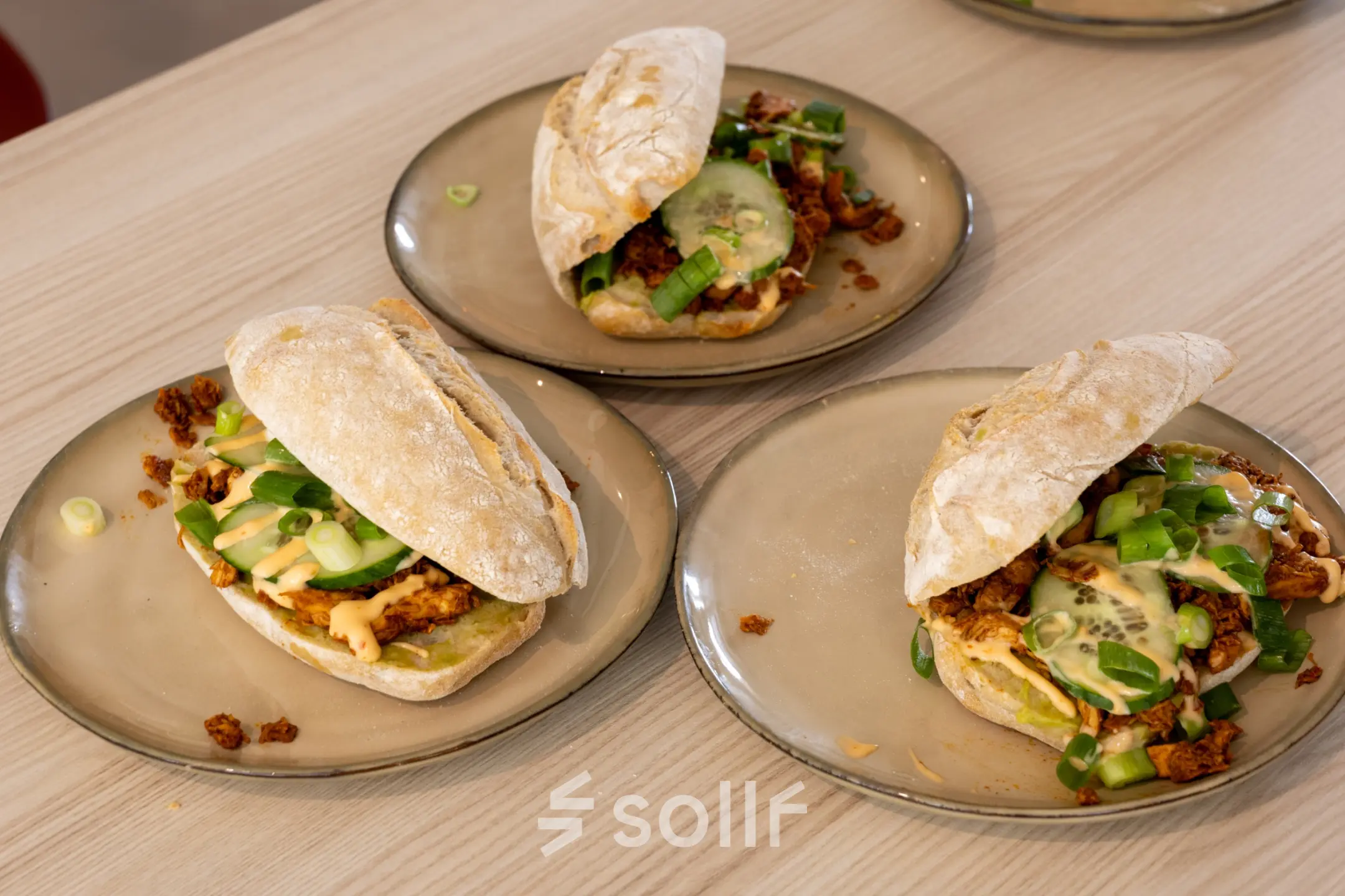 Three plates with sandwiches featuring a variety of toppings on a wooden table.