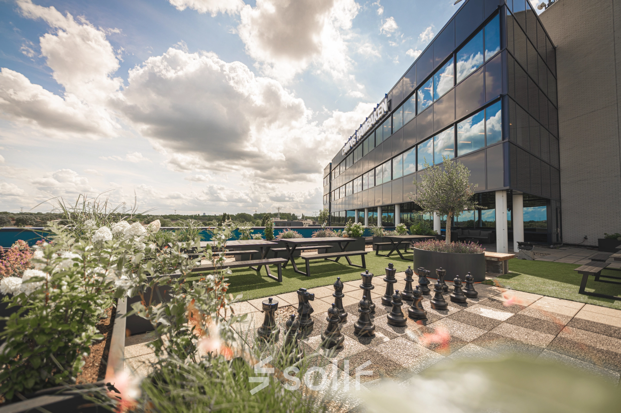 Modern office to rent at Luttenbergweg 8, Amsterdam South East, featuring an outdoor area with picnic tables and a large chessboard set against a reflective building facade.