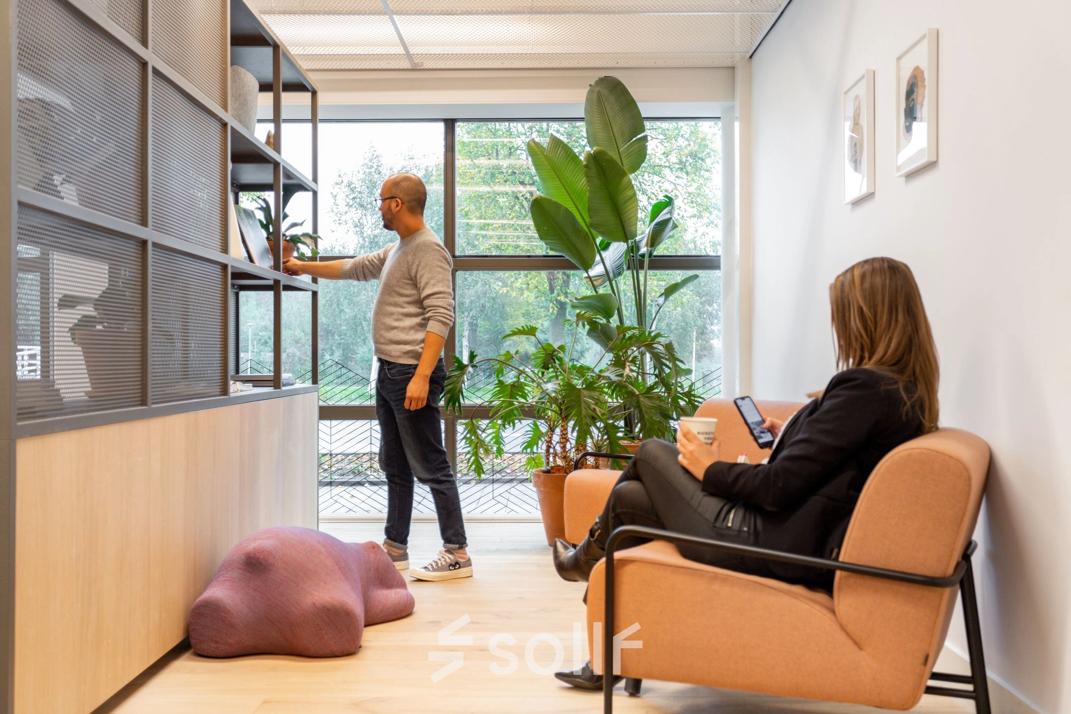 A modern office at Haarlemmerweg 331, Amsterdam West, with a person browsing shelves and another seated with a tablet. Ideal for office space rental.