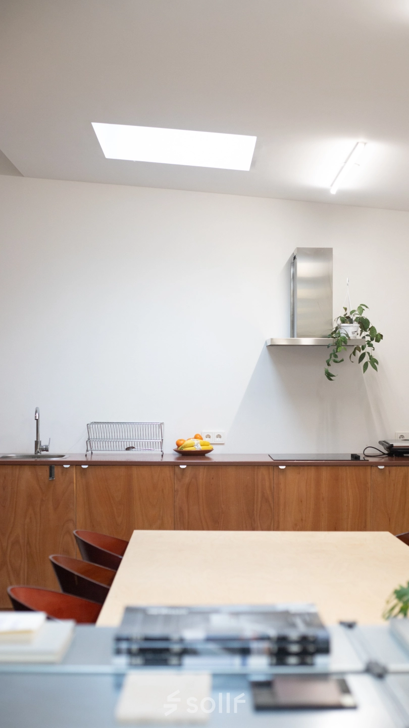 Modern, minimalistic kitchen space in an office to rent at Hondiusstraat 7H, Amsterdam West. Features a sleek counter, wooden cabinets, and a skylight for natural light.