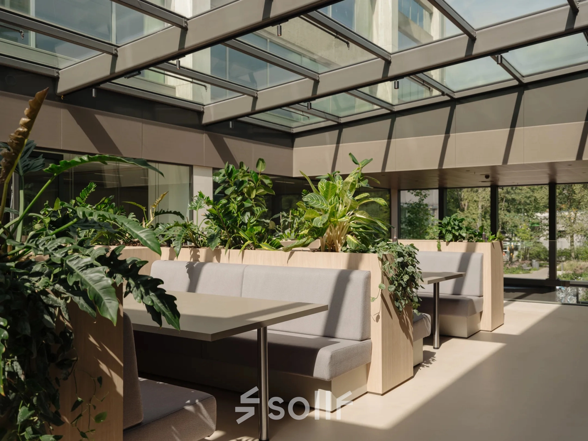 Bright and modern office space rental at Nachtwachtlaan 20, Amsterdam West, featuring a skylight, plants, and seating booths for a refreshing work atmosphere.