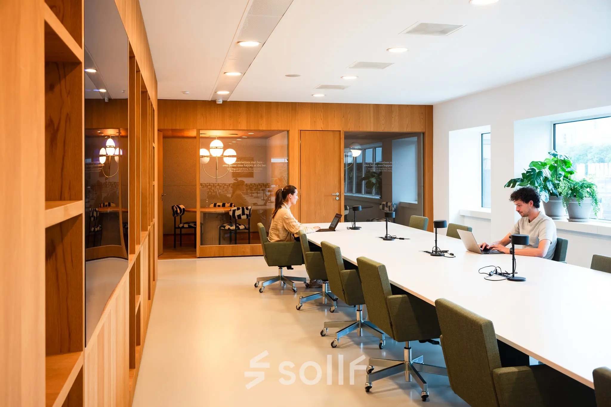 Modern office space at Barbara Strozzilaan 101, Amsterdam Zuidas, featuring a well-lit conference room with large table, office chairs, and two people working on laptops.