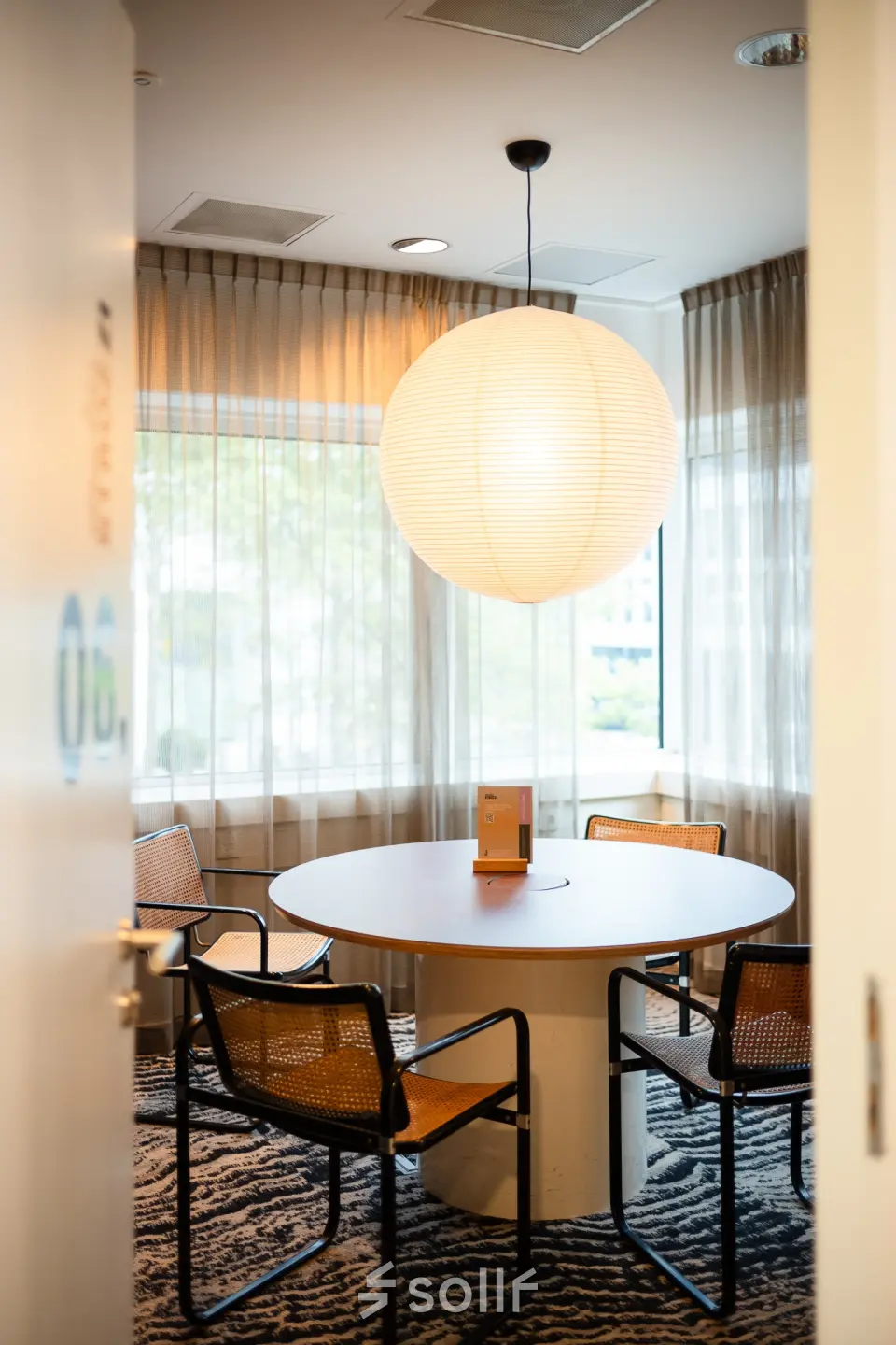 Cozy office space with a round table and four chairs under a large hanging lamp at Barbara Strozzilaan 101, Amsterdam Zuidas, ideal for small meetings. Perfect spot for office space rental.