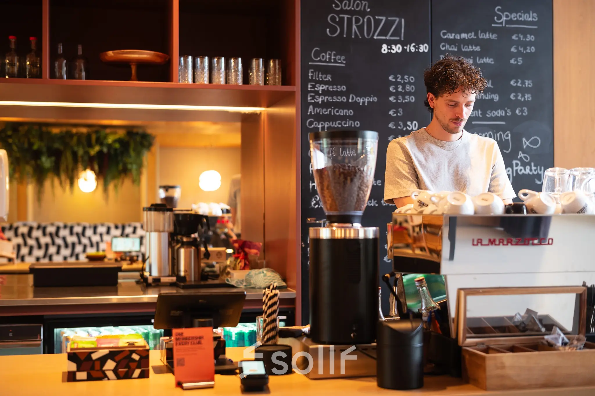 Man working at a coffee bar inside an office space at Barbara Strozzilaan 101, Amsterdam Zuidas. The setting offers a cozy environment for office space rental.