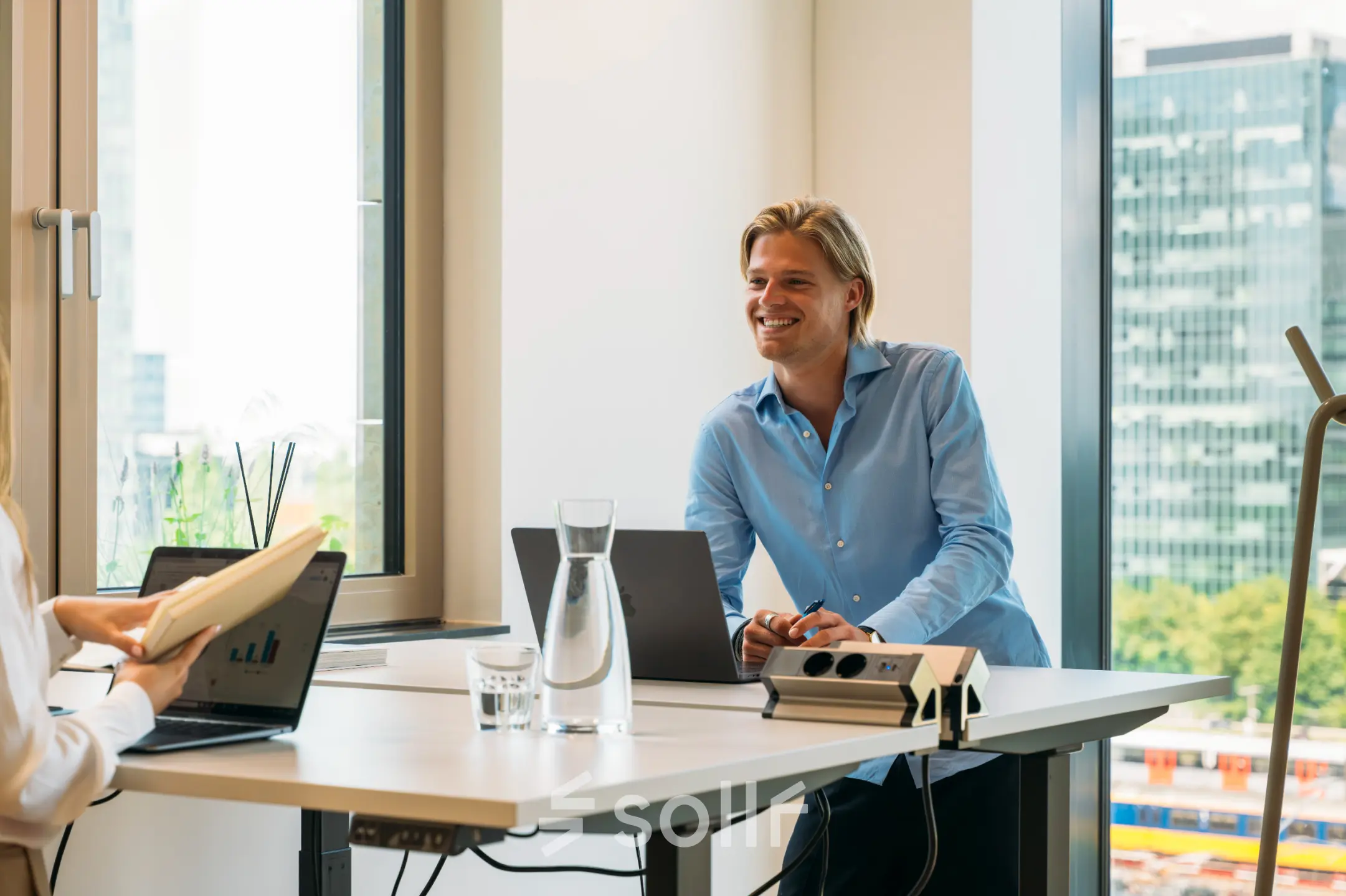Two professionals are engaged in a discussion over laptops and documents in a bright, modern office space. Ideal for those seeking office space rental in Amsterdam Zuidas.