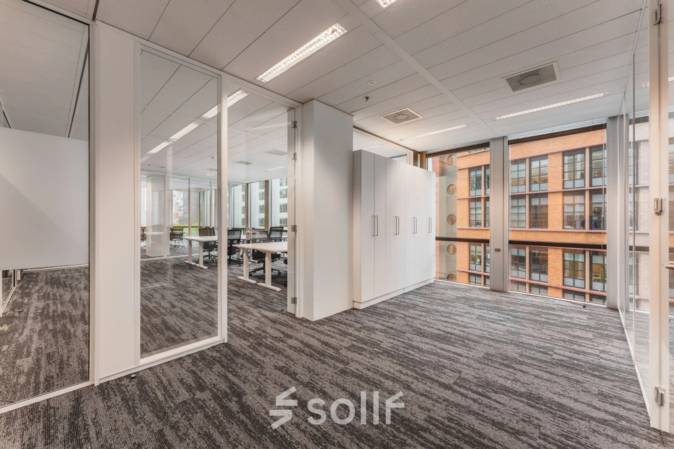 Bright office space with glass partitions, modern lighting, and visible cabinets, ideal for rent in Amsterdam Zuidas.