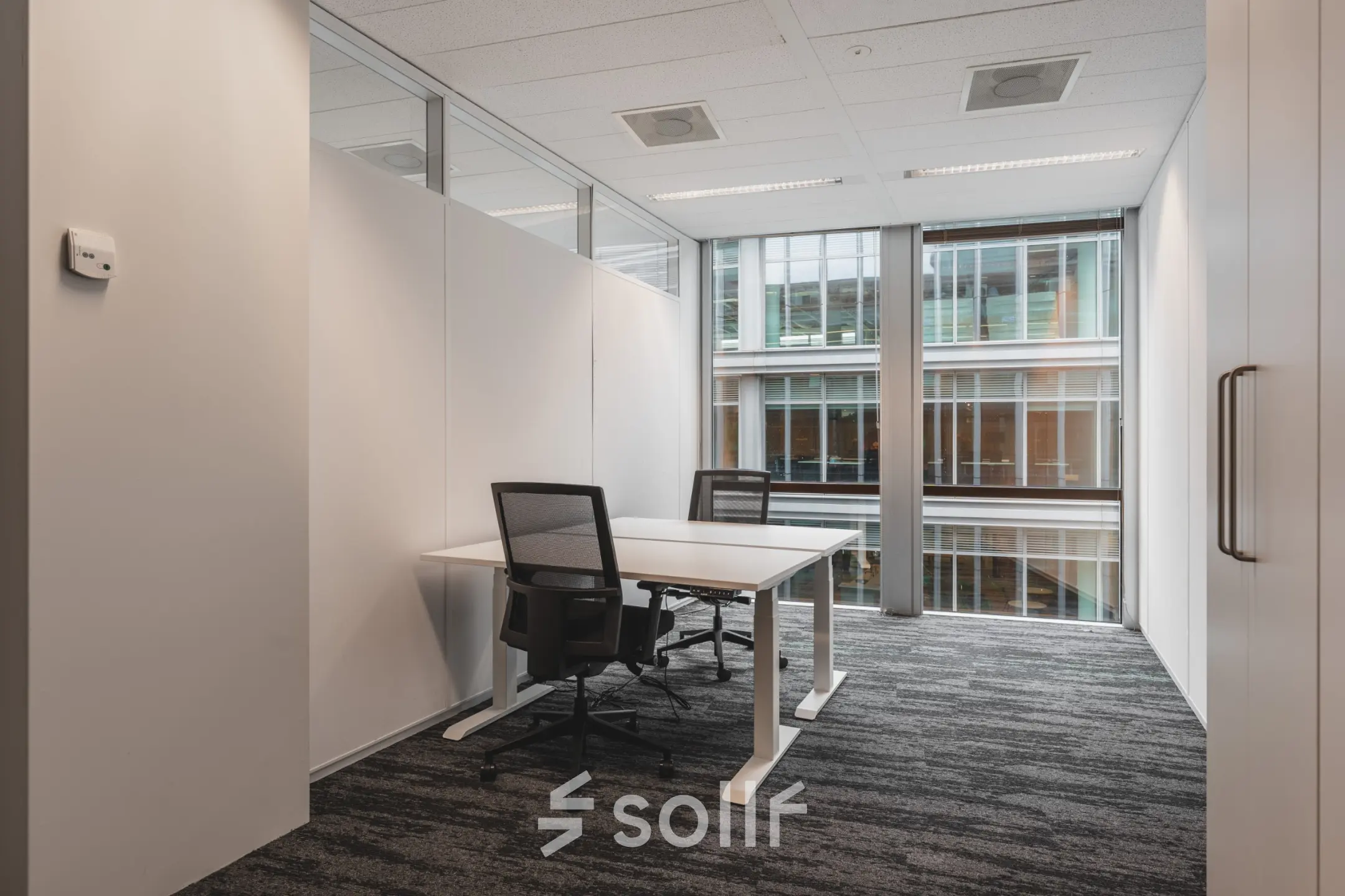 Minimalist office space for rent at Claude Debussylaan 10 in Amsterdam Zuidas, featuring a large desk with chairs against a glass wall.