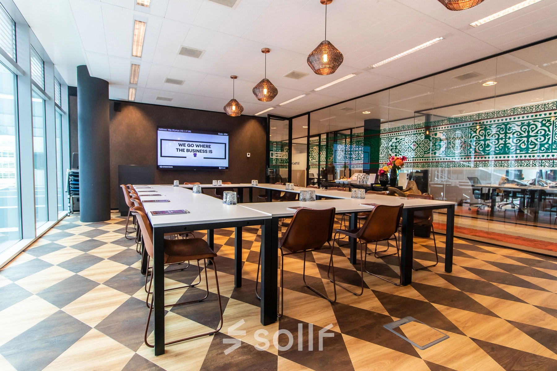 Modern office space for rent at Claude Debussylaan 7-29, Amsterdam Zuidas, featuring a stylish meeting area with geometric flooring, glass partitions, and trendy light fixtures.