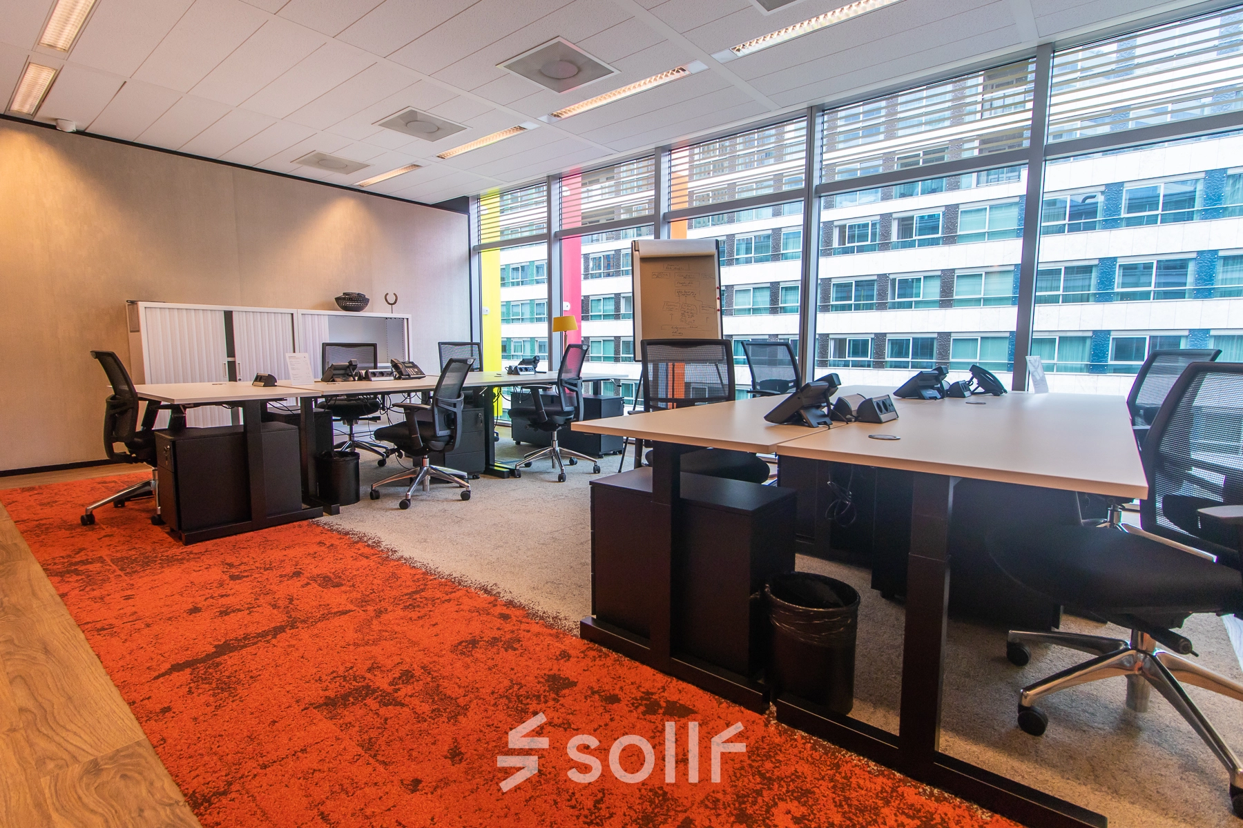 Modern office space with large windows and multiple workstations available for rent at Claude Debussylaan 7-29, Amsterdam Zuidas. The bright interior features desks and chairs, ideal for office space rental.
