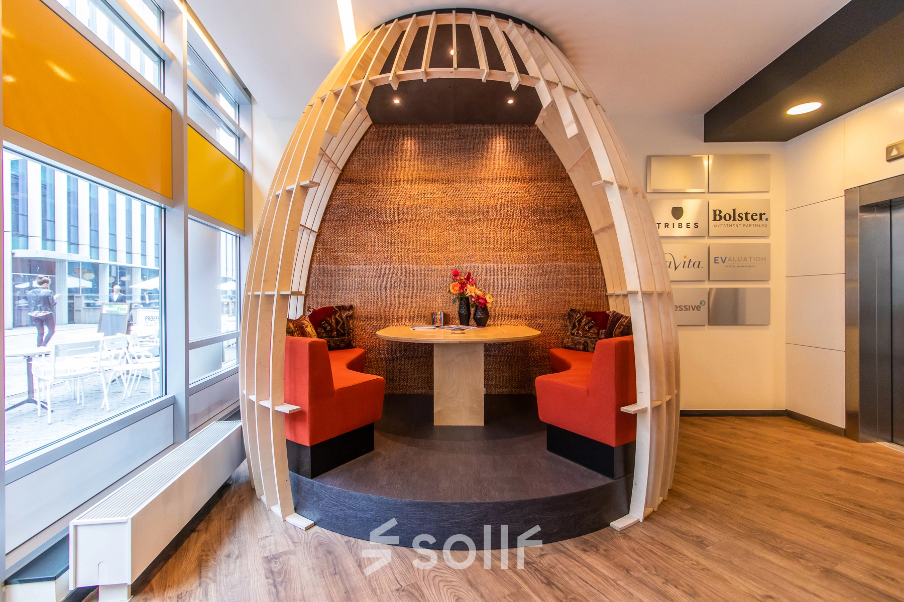 Cozy office space rental in Amsterdam Zuidas featuring a unique circular seating area with red cushioned benches and a wooden table, perfect for collaborative work sessions.