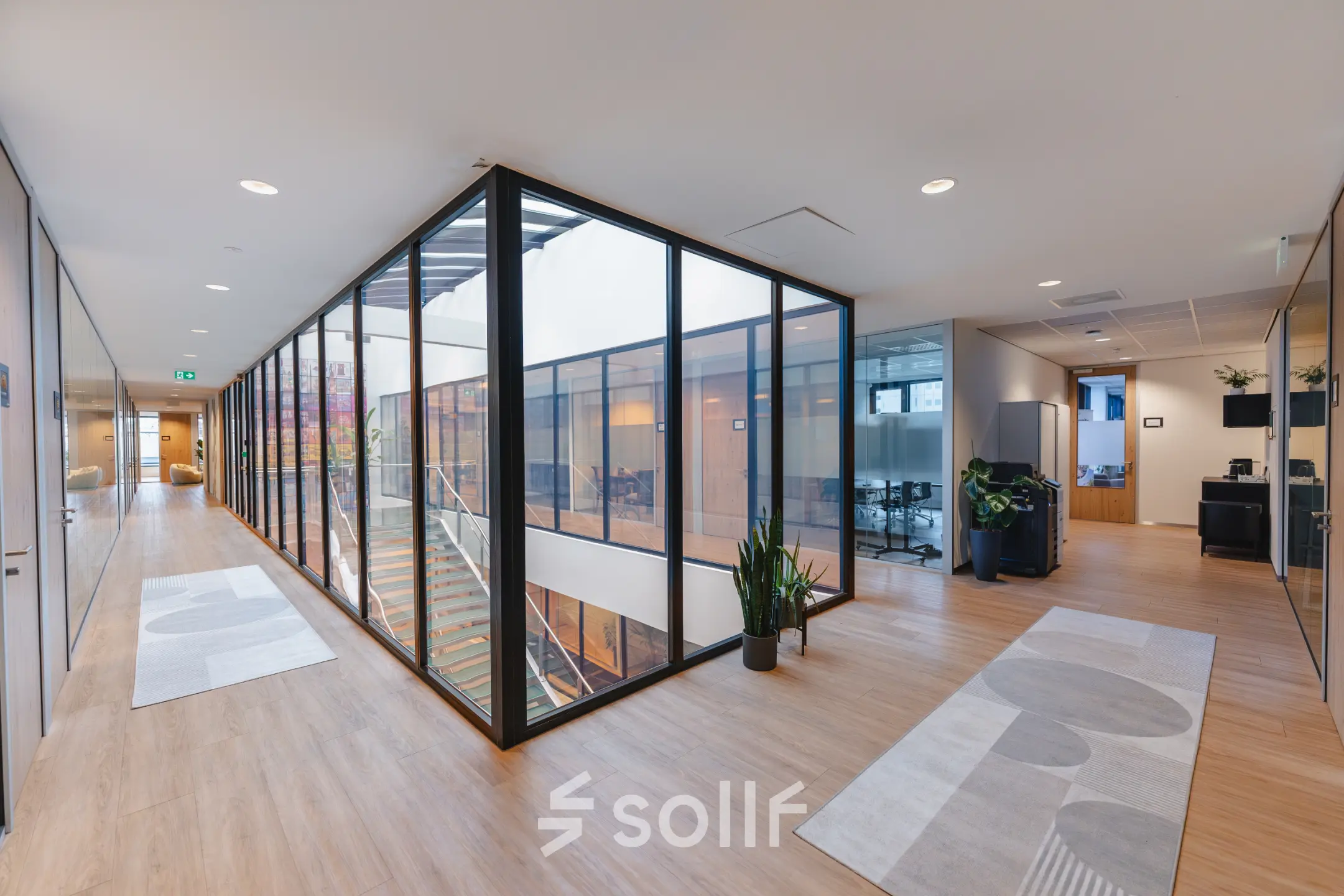 Modern office space at De Boelelaan 30, Amsterdam Zuidas, featuring glass walls, wooden flooring, and a view into conference rooms. Ideal for office space rental.