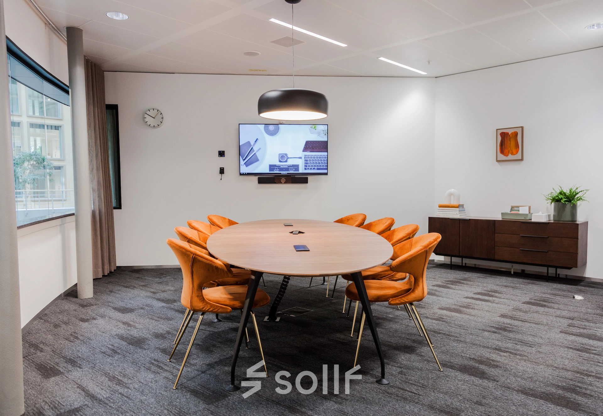 Modern office to rent at Fred. Roeskestraat 100 in Amsterdam Zuidas featuring a furnished conference room with a round table, orange chairs, and a TV screen for presentations.