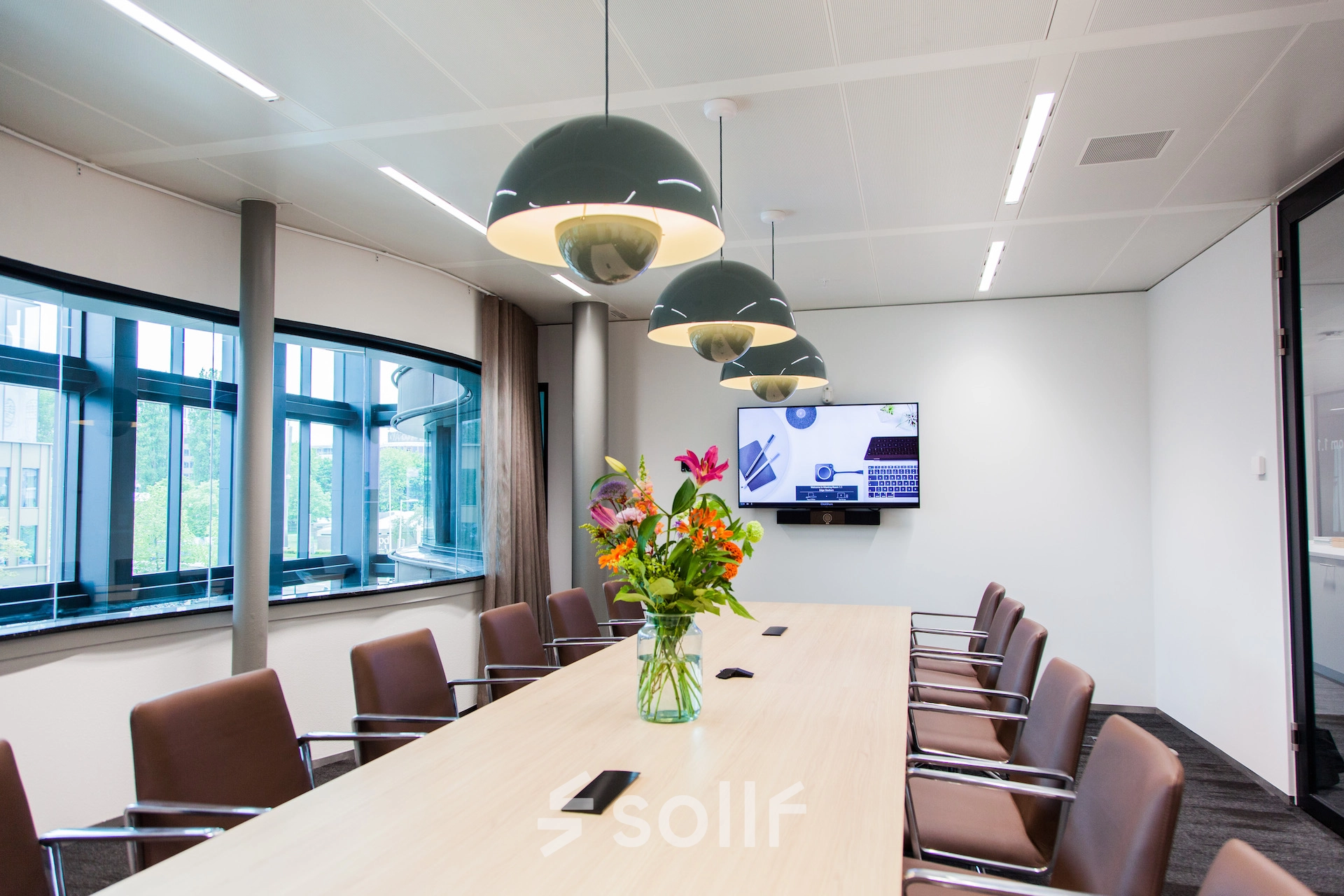 Modern conference room at Fred. Roeskestraat 100, Amsterdam Zuidas, featuring a long table with chairs, decorative lighting, and a wall-mounted screen, perfect for office space rental.