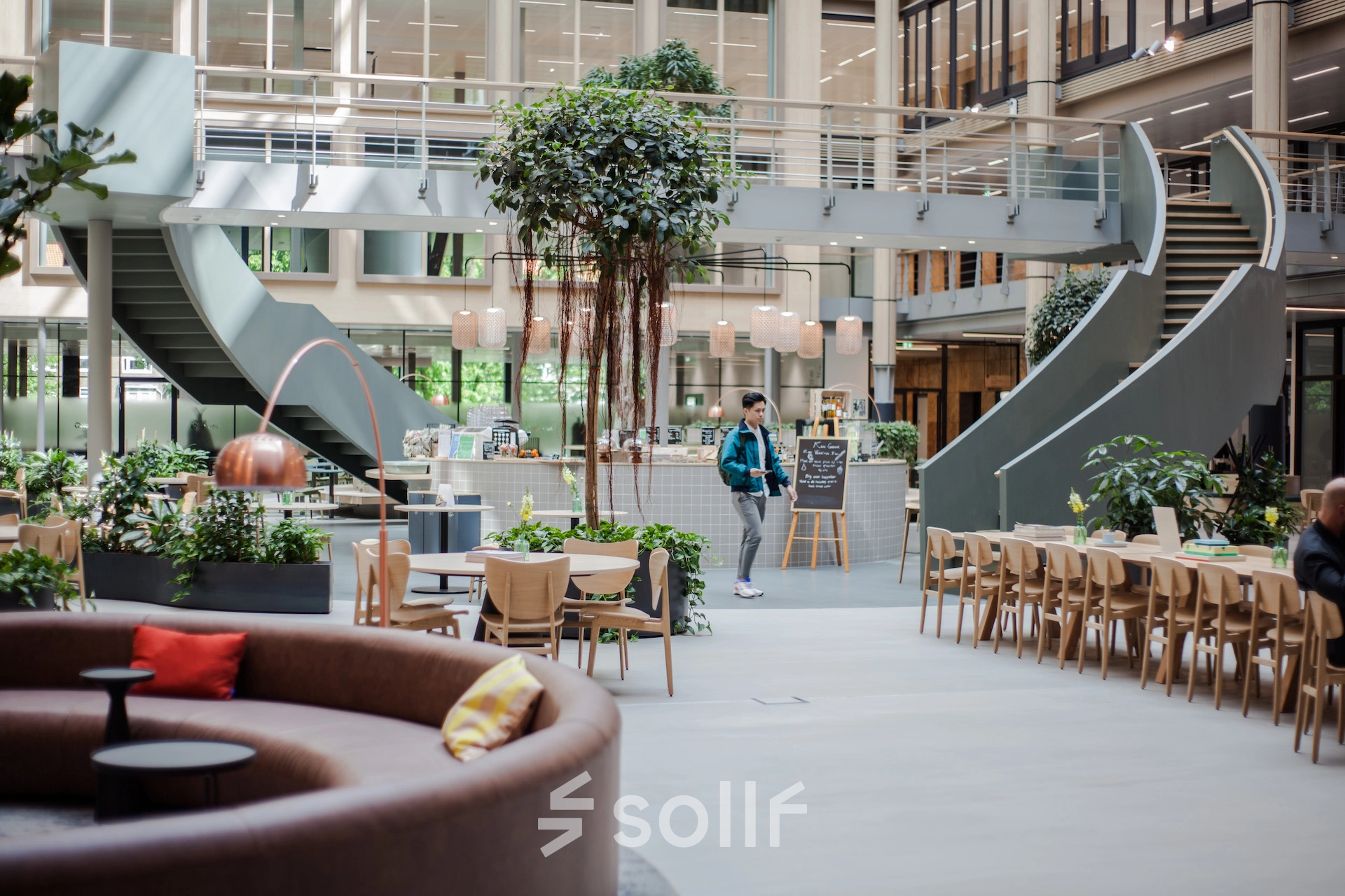 Open office space in Amsterdam Zuidas at Fred. Roeskestraat 100, featuring modern furniture and a central lounge area. People are engaged in business discussions and activities, adding to the vibrant atmosphere.