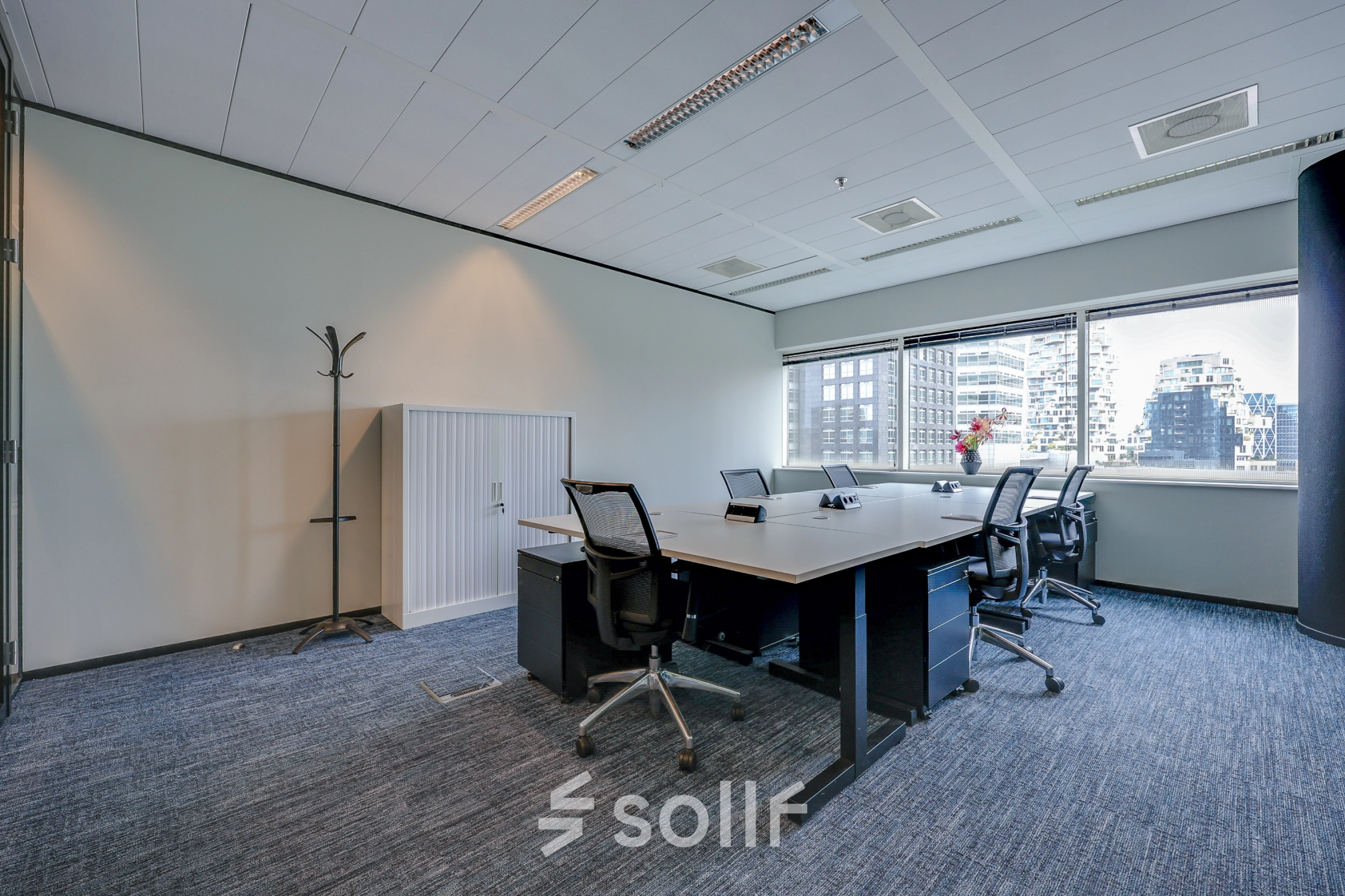 Bright office space with a large window offering city views, featuring a conference table and office chairs, perfect for meetings. Suitable for office space rental in Amsterdam Zuidas.