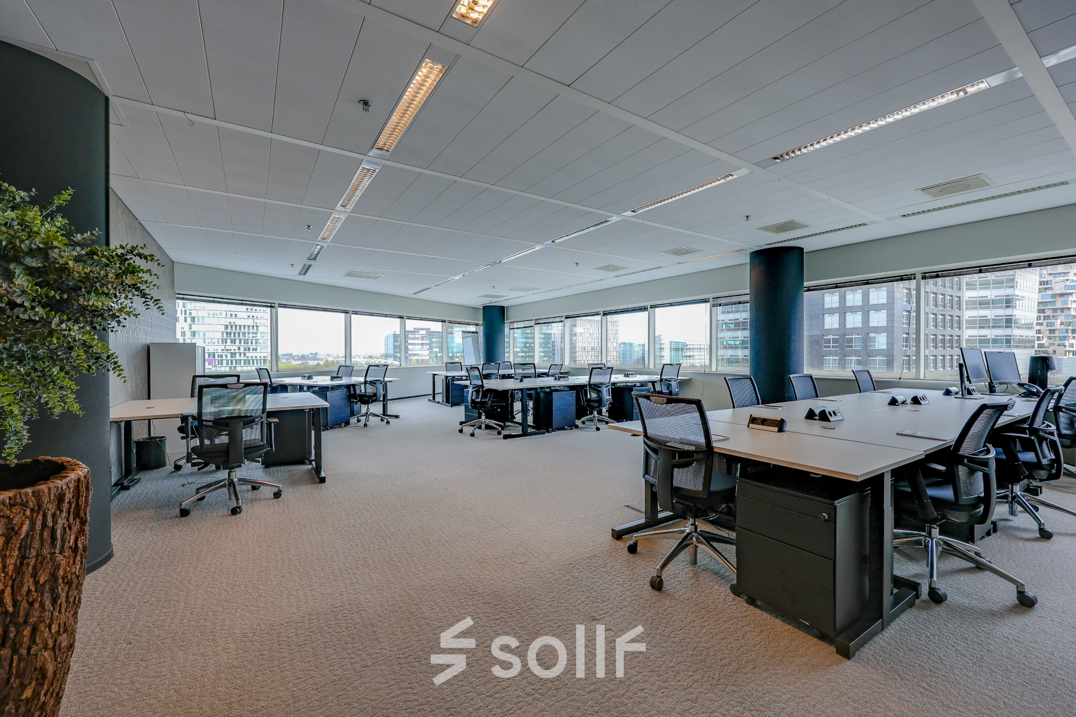 Bright office space available for rent at Gustav Mahlerplein, Amsterdam Zuidas, featuring modern desks, chairs, and large windows offering city views.