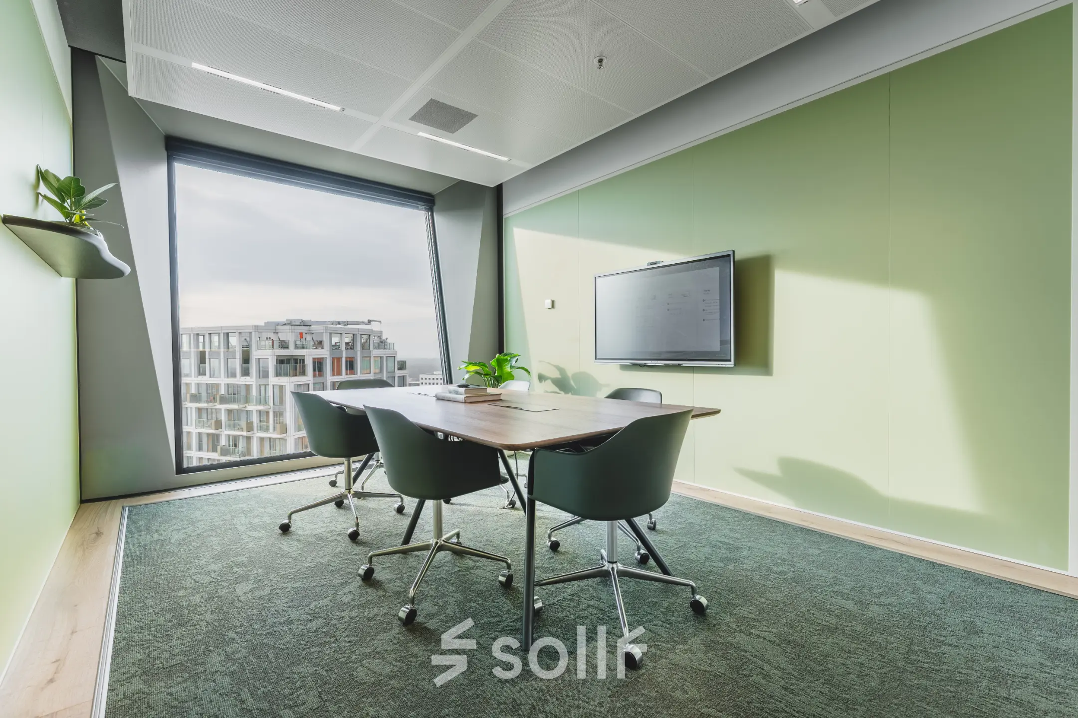 Bright office to rent in Amsterdam Zuidas with a conference table, chairs, large window, and wall-mounted TV, ideal for office space rental.