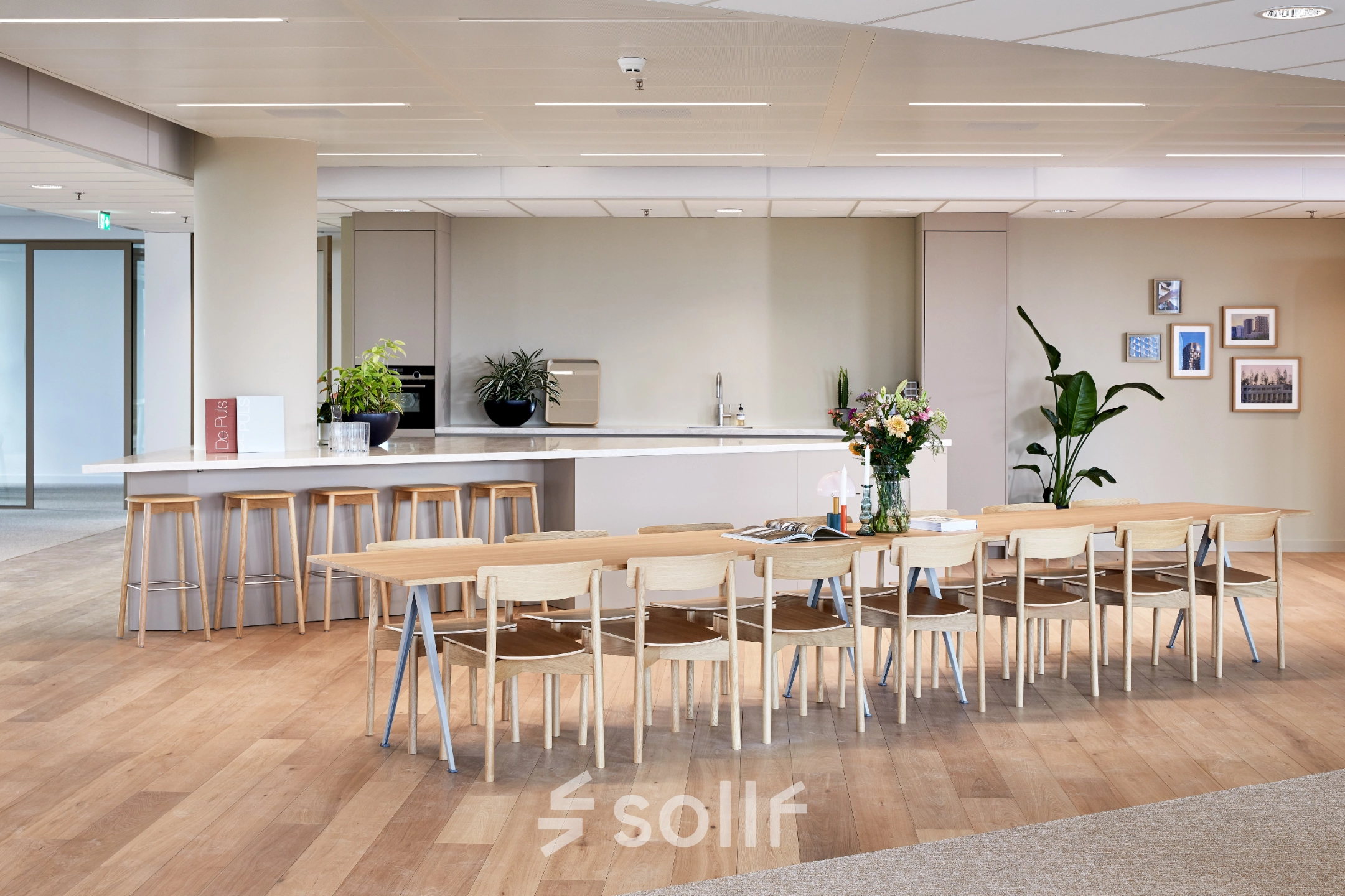 Spacious furnished office area in Amsterdam Zuidas, featuring a long table with chairs, bar stools, and a kitchenette. Ideal for office space rental at Hildegard Von Bingenstraat 44.