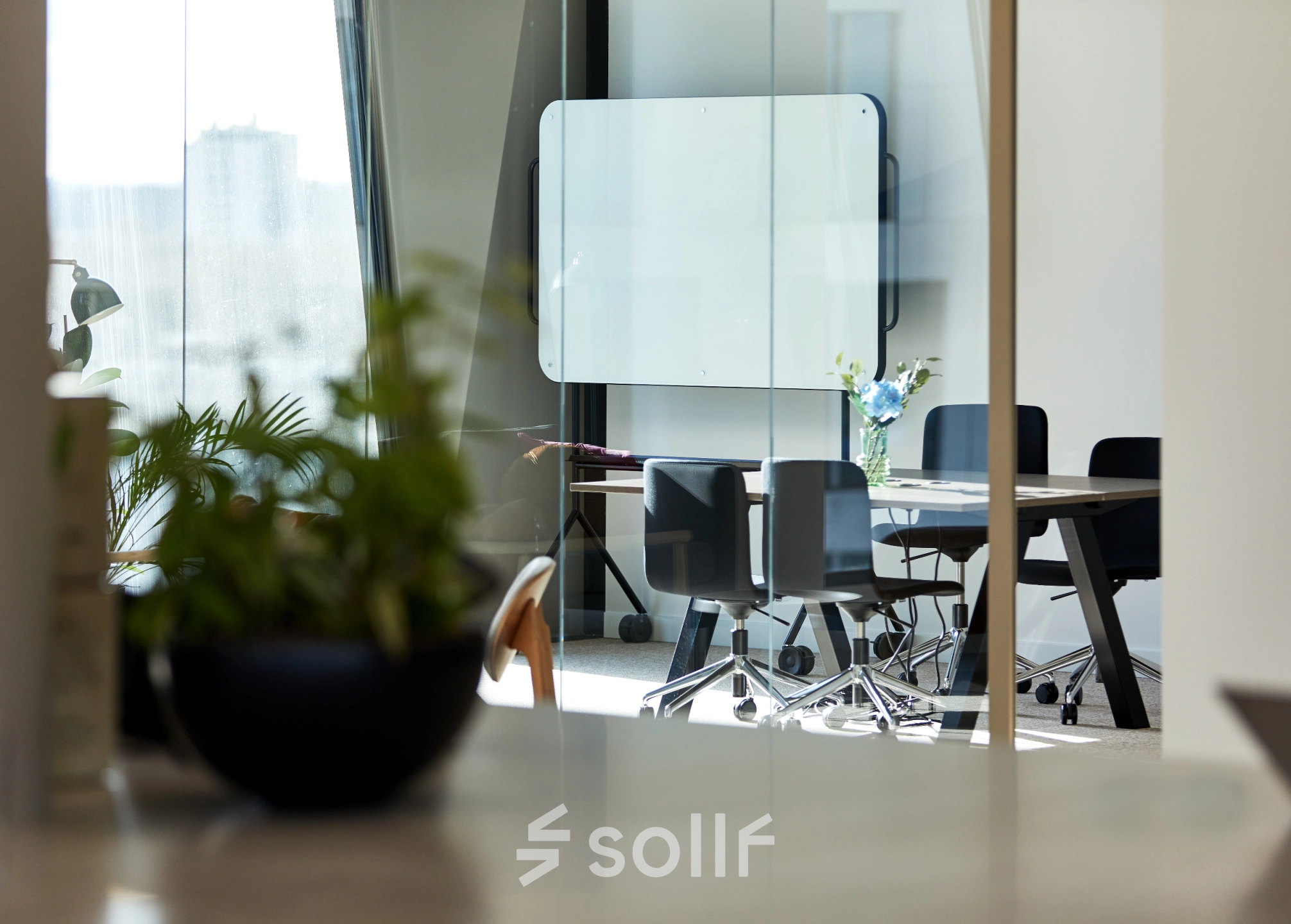 Modern office space in Amsterdam Zuidas with a bright meeting area, featuring sleek chairs, a glass table, and green plants, ideal for office space rental.