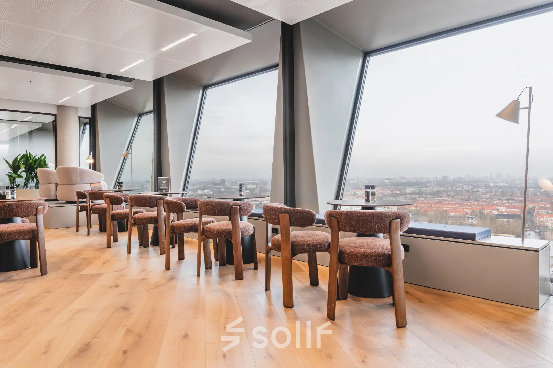 Bright office space with large windows overlooking Amsterdam Zuidas, featuring modern wooden furniture and city views. Ideal office space rental at Hildegard Von Bingenstraat 44.