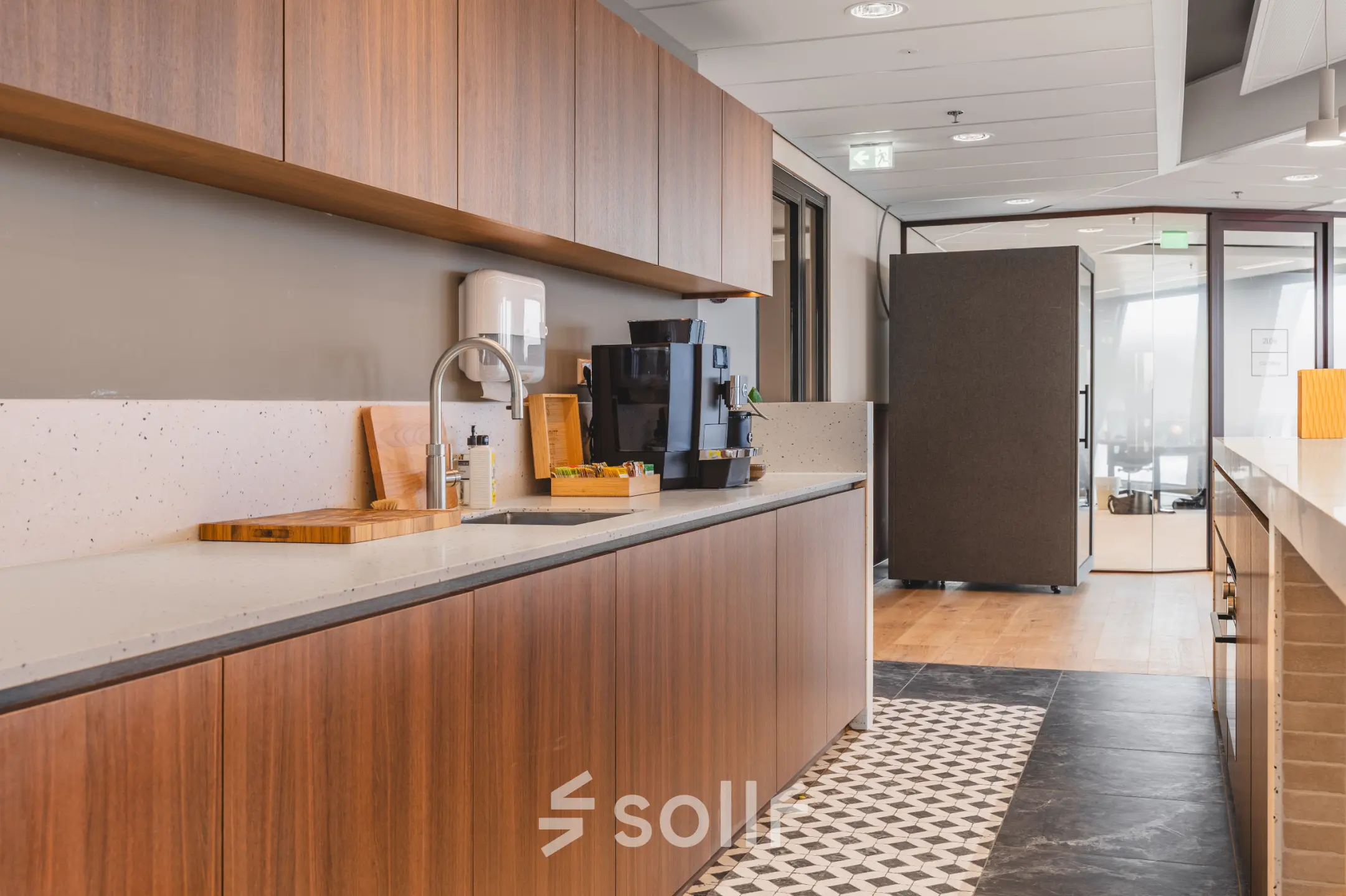 Modern office pantry in Amsterdam Zuidas at Hildegard Von Bingenstraat 44, featuring wooden cabinetry, a sleek countertop, and a coffee machine, perfect for office space rental needs.