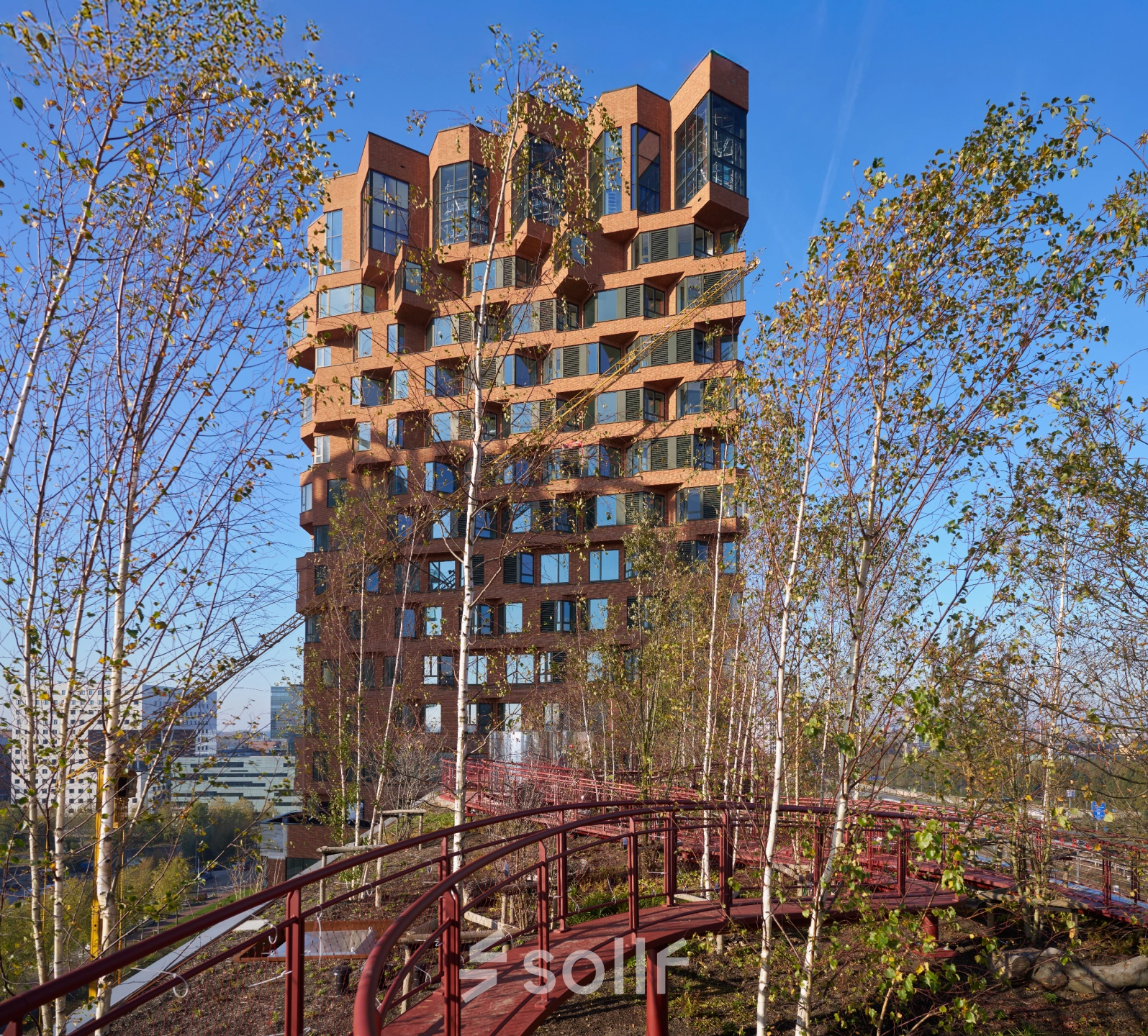 Exterior view of an office building at Hildegard Von Bingenstraat 44, Amsterdam Zuidas. Office space rental available with a unique architectural design surrounded by trees and walkways.