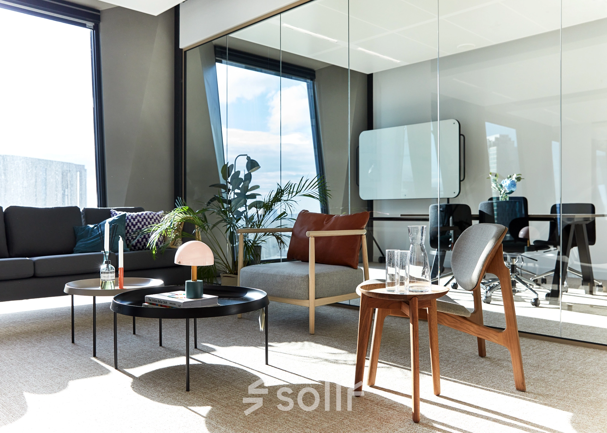 Modern office space for rent in Amsterdam Zuidas with stylish furniture, glass walls, and natural light through large windows. Ideal for office space rental with comfortable seating and plants.