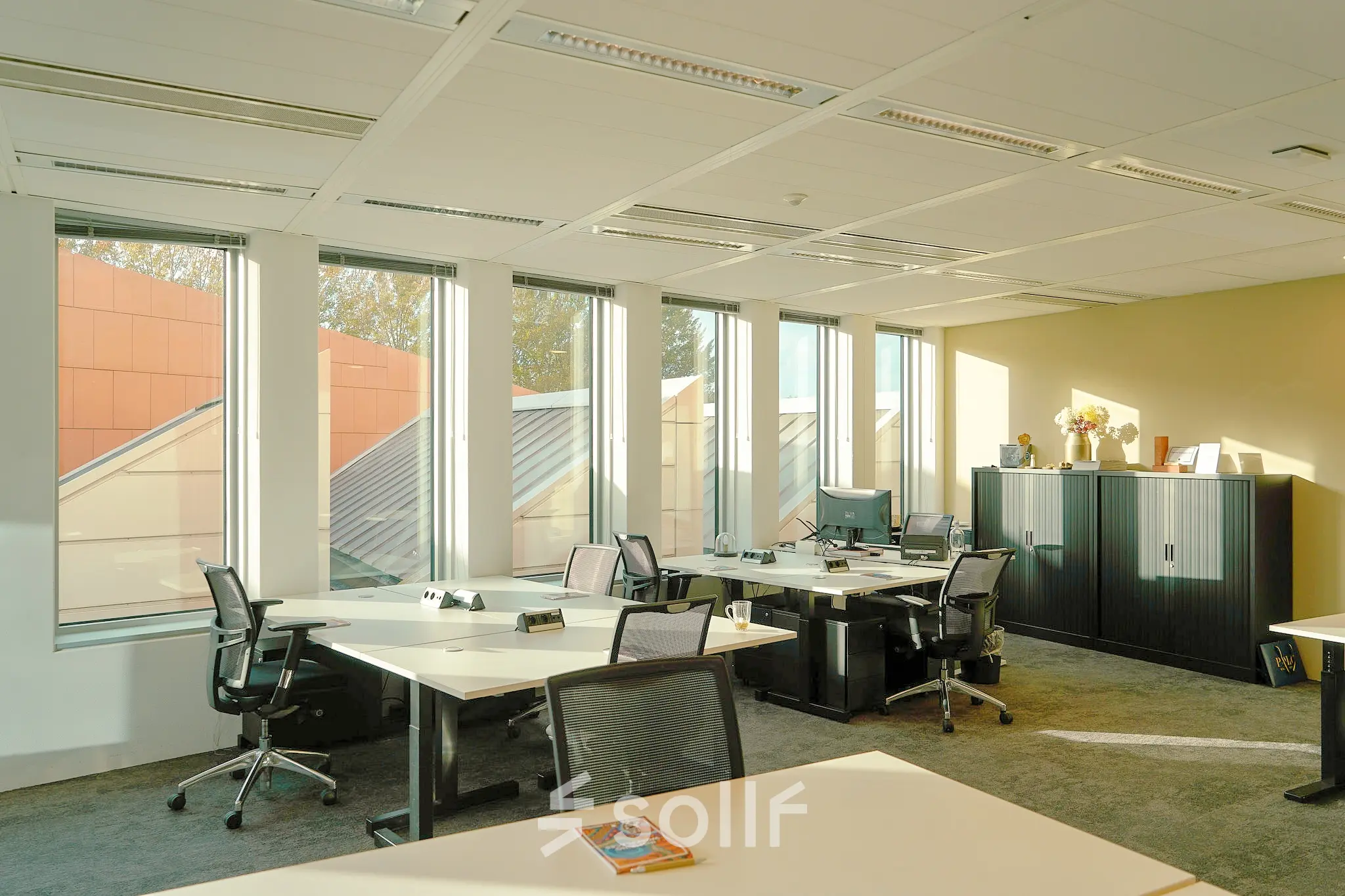 Bright office space with desks and chairs in Amsterdam Zuidas, available for rent. Features large windows and modern furnishings.