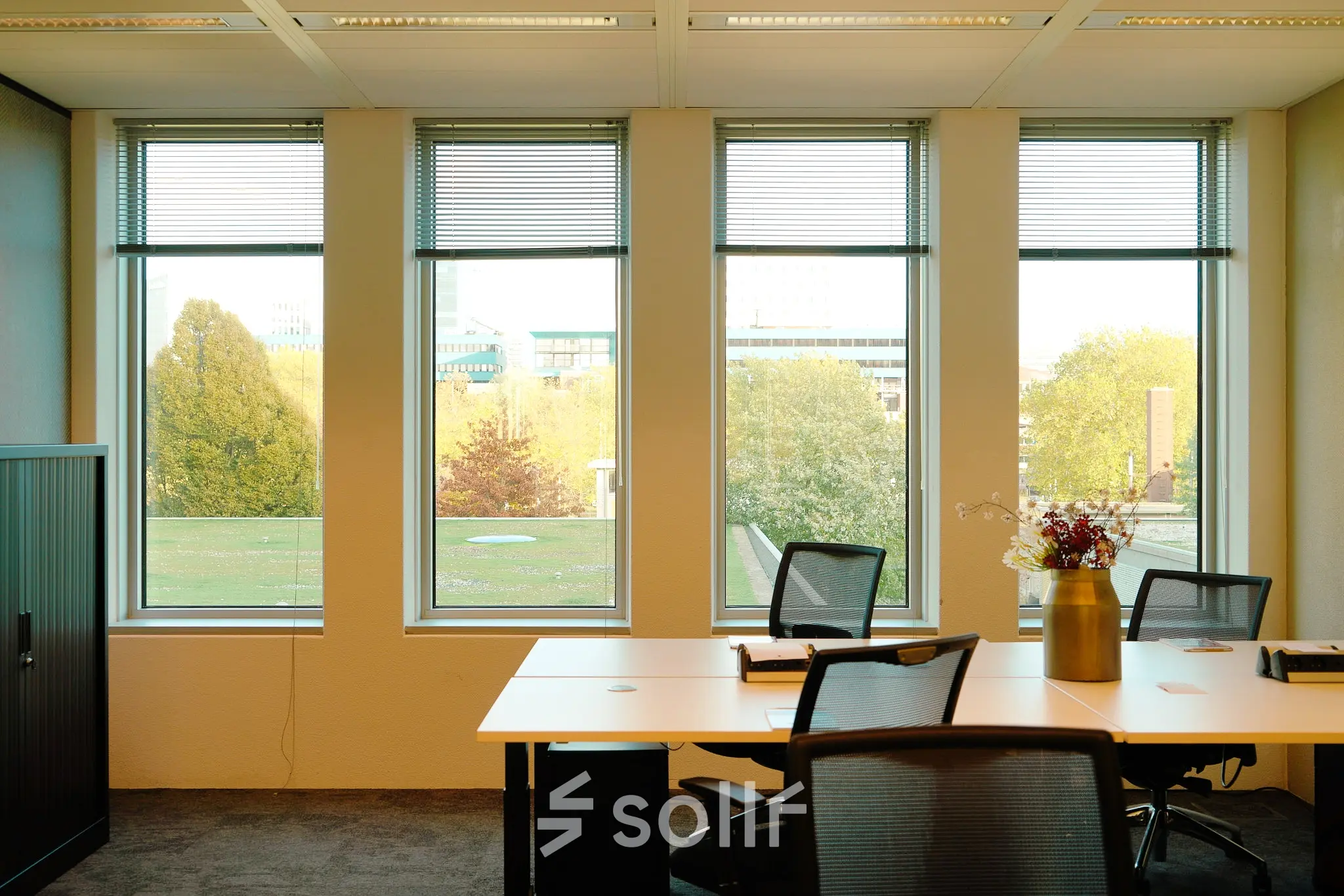 Bright office space at Jachthavenweg 109 in Amsterdam Zuidas featuring modern furnishings and large windows with a view of greenery. Ideal office to rent for a dynamic work environment.