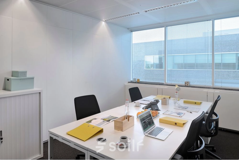Bright office space with a large window, four desks, chairs, and office supplies in Antwerp Center, ideal for rent office space seekers.