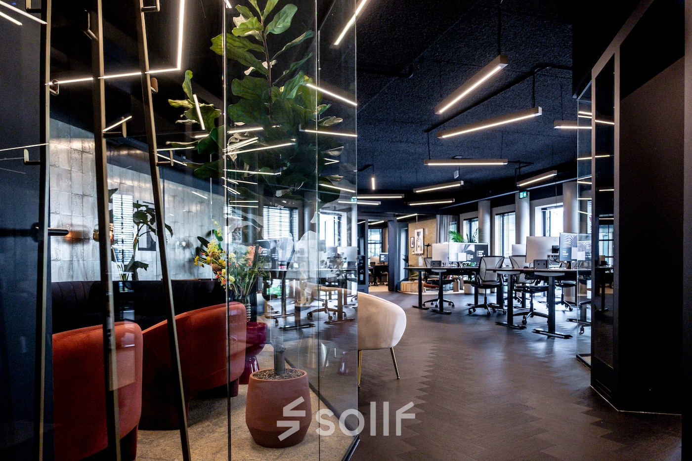 Modern office space with glass walls and stylish lighting; a mix of seating and workstations. Ideal for office space rental.