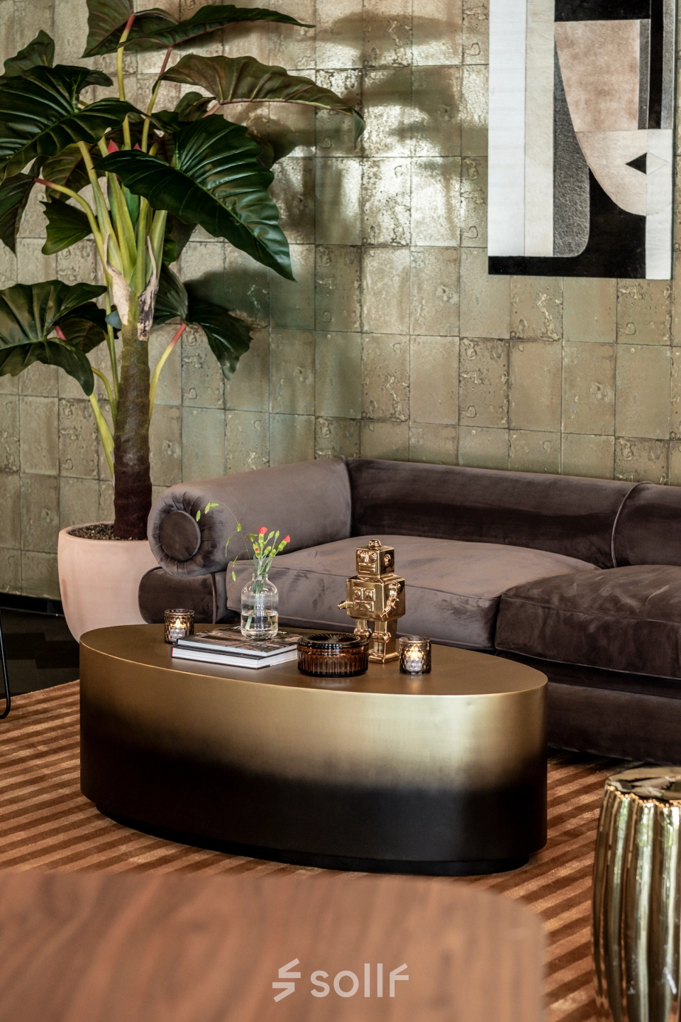 A stylish office lounge with a plush sofa, coffee table, decorative plant, and abstract artwork, located at Lange Amerikaweg 55-61, Apeldoorn. Ideal for office space rental.