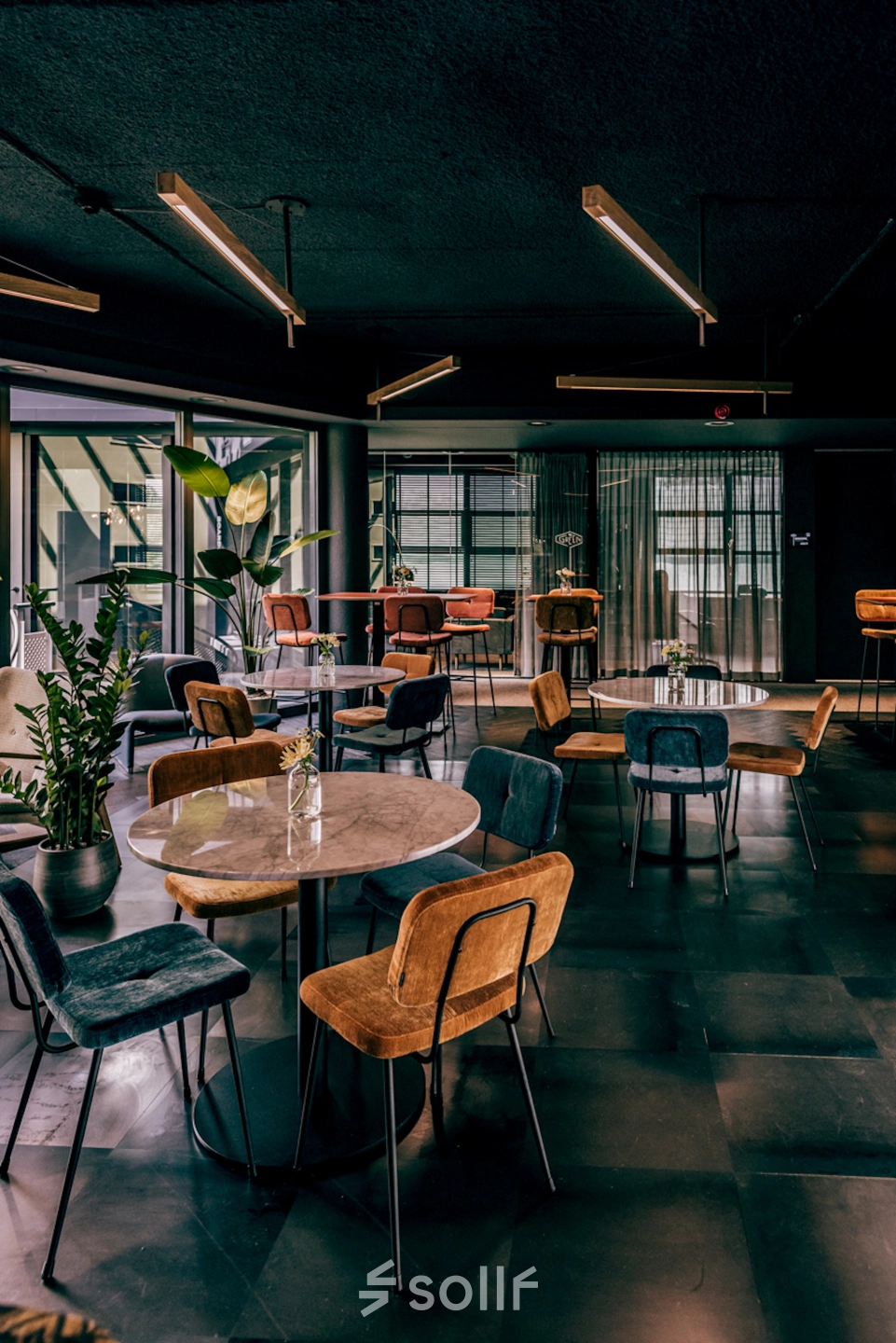 Stylishly furnished office space with round tables, multicolored chairs, and potted plants, ideal for rent at Lange Amerikaweg 55-61, Apeldoorn.