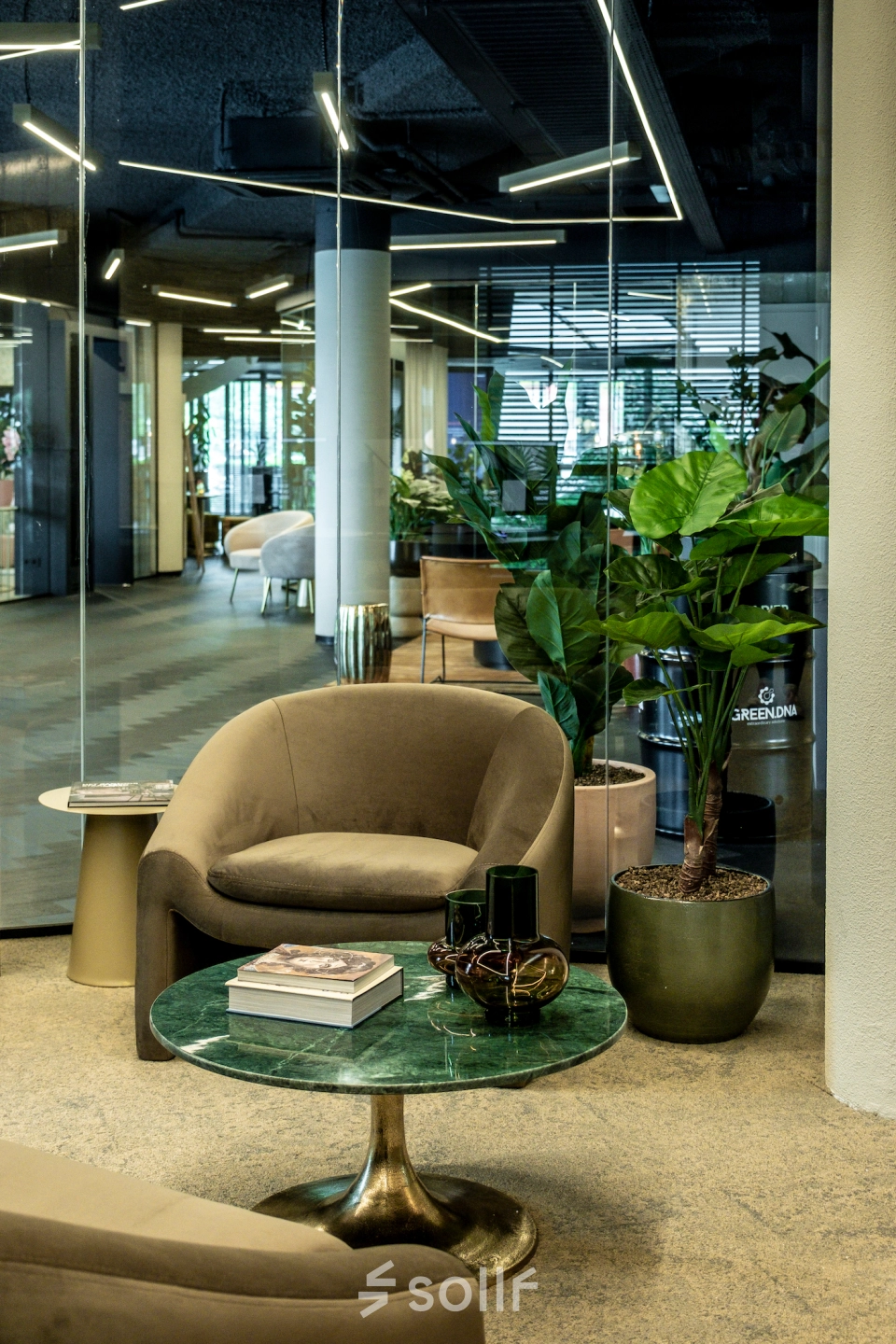 Rent office space at Lange Amerikaweg 55-61 in Apeldoorn featuring a cozy furnished lounge with glass walls, stylish seating, and greenery, ideal for office space rental.