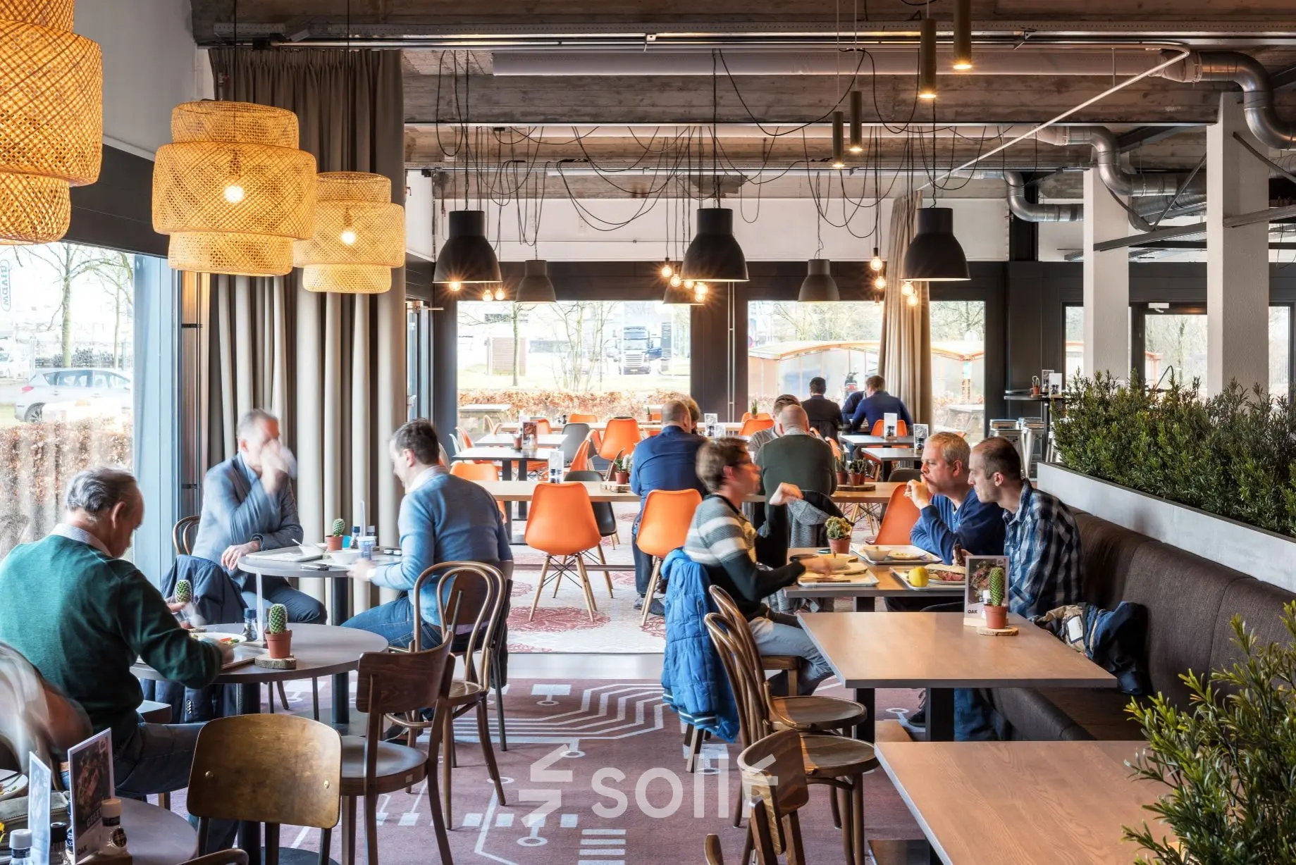 Lively office space at Oude Apeldoornseweg 41-45, Apeldoorn, featuring people engaged in discussions and dining at wooden tables with vibrant chairs.