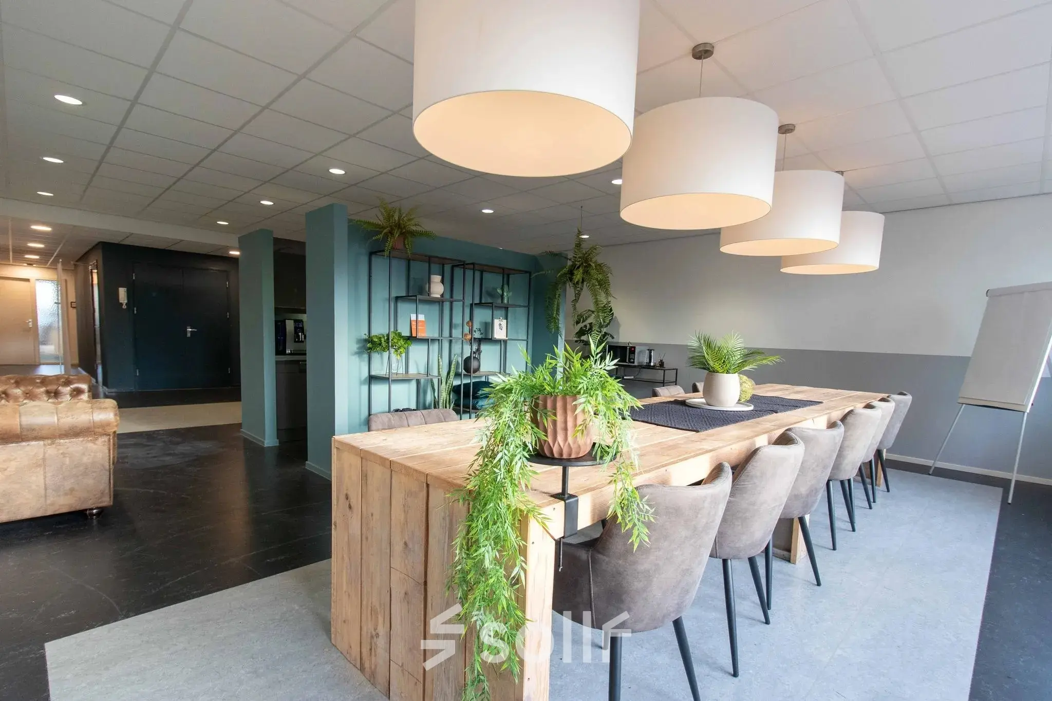 Spacious, modern office interior with a large wooden table surrounded by chairs and lush greenery, ideal for office space rental at Prins Willem-Alexanderlaan 401, Apeldoorn.